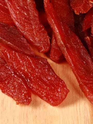 A pile of homemade salmon jerky on a wooden cutting board.