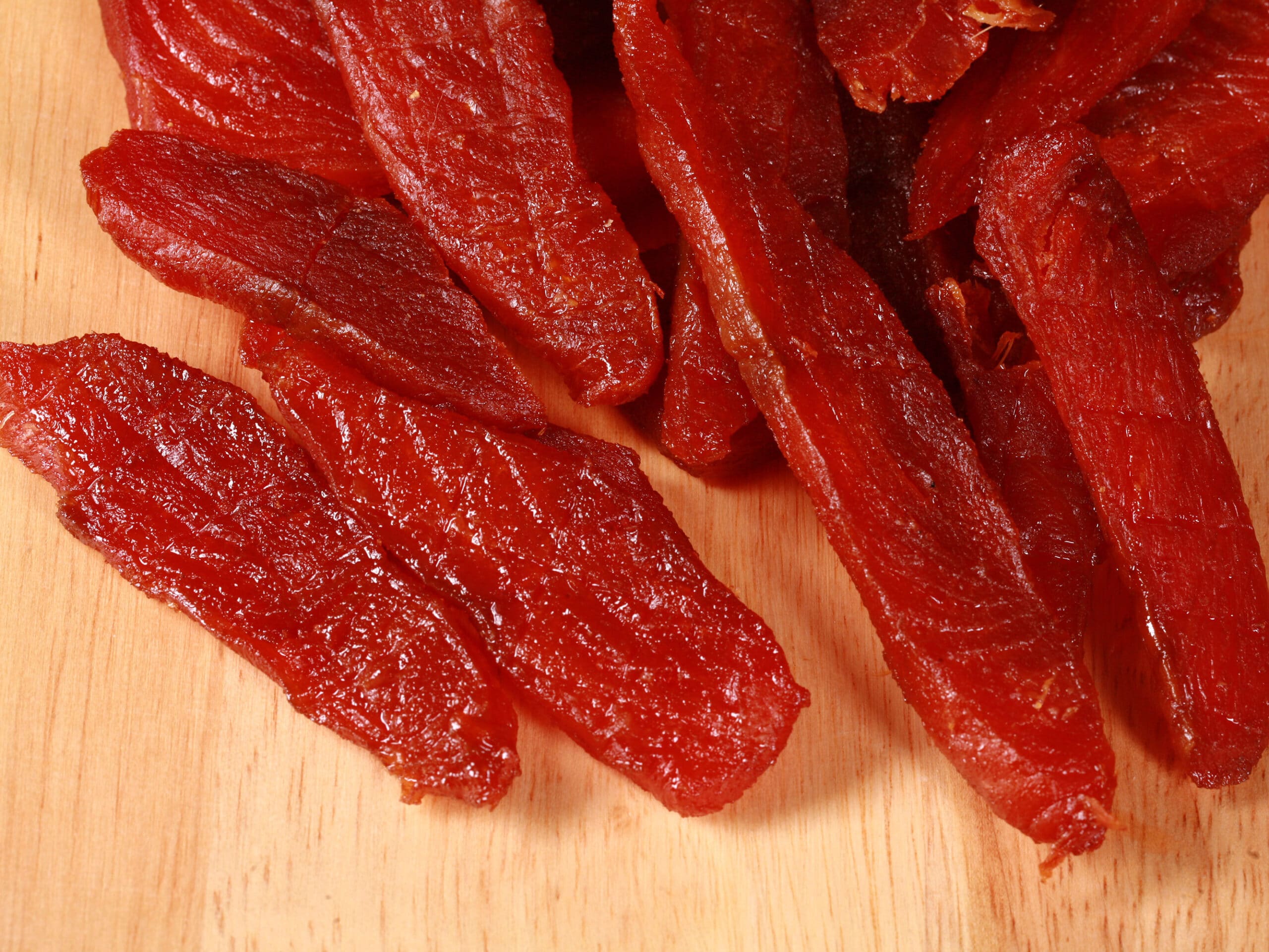 A pile of homemade salmon jerky on a wooden cutting board.