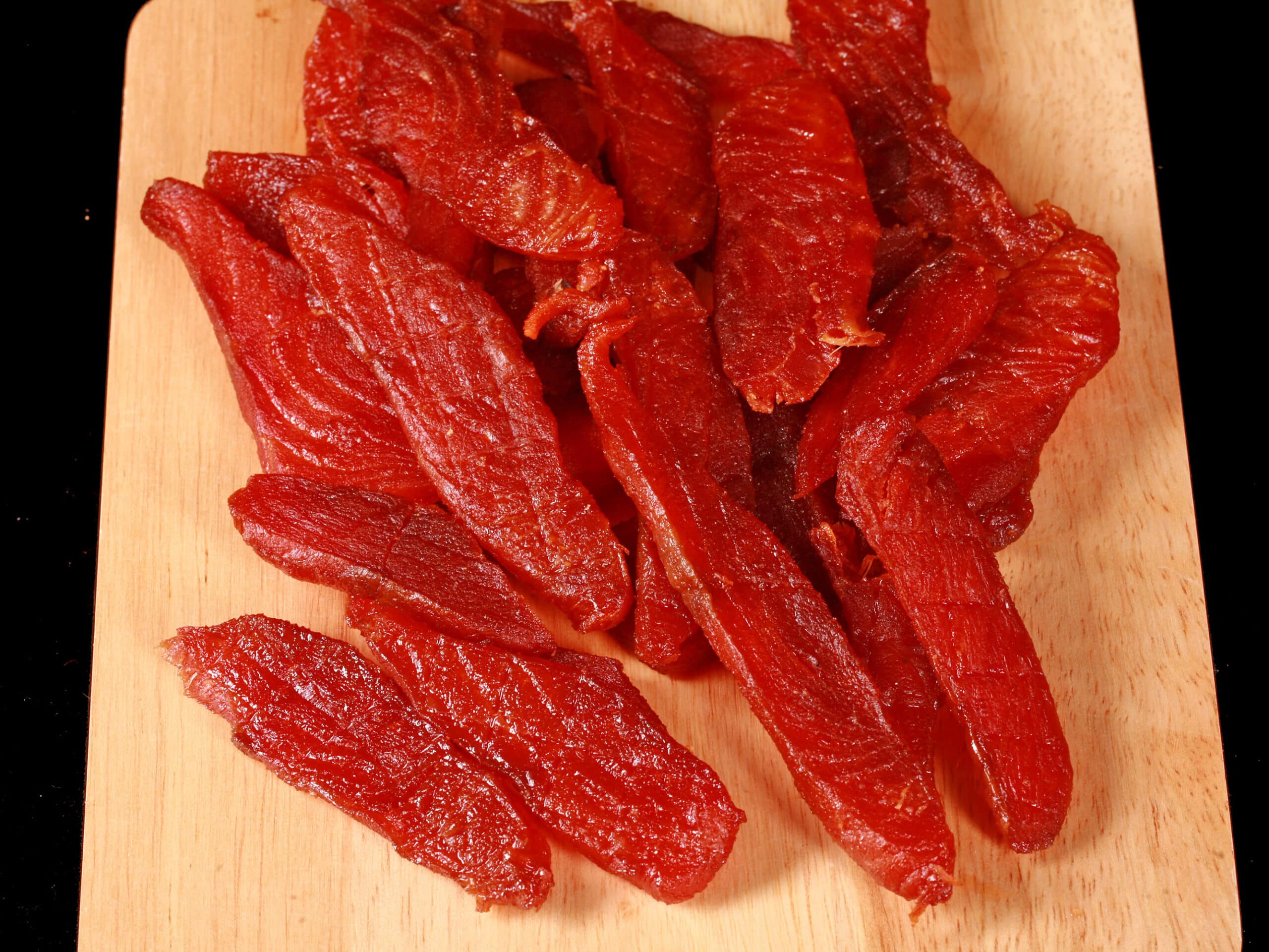 A pile of homemade maple salmon jerky on a wooden cutting board.