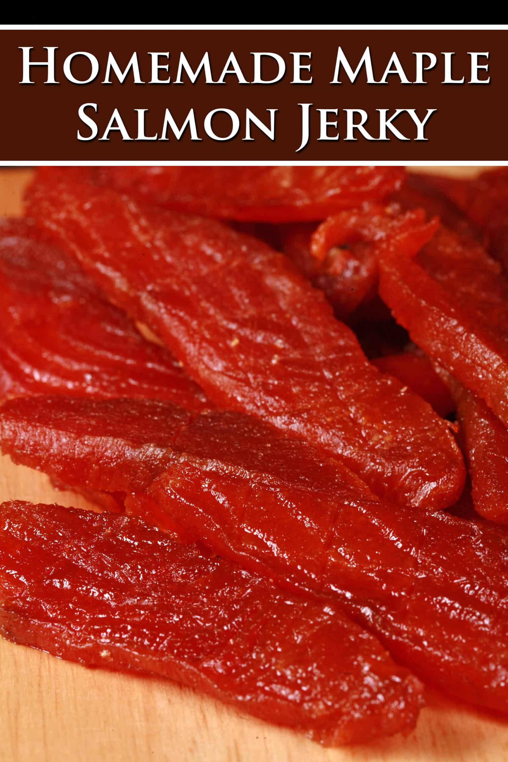 A pile of homemade salmon jerky on a wooden cutting board. Overlaid text says homemade maple salmon jerky.