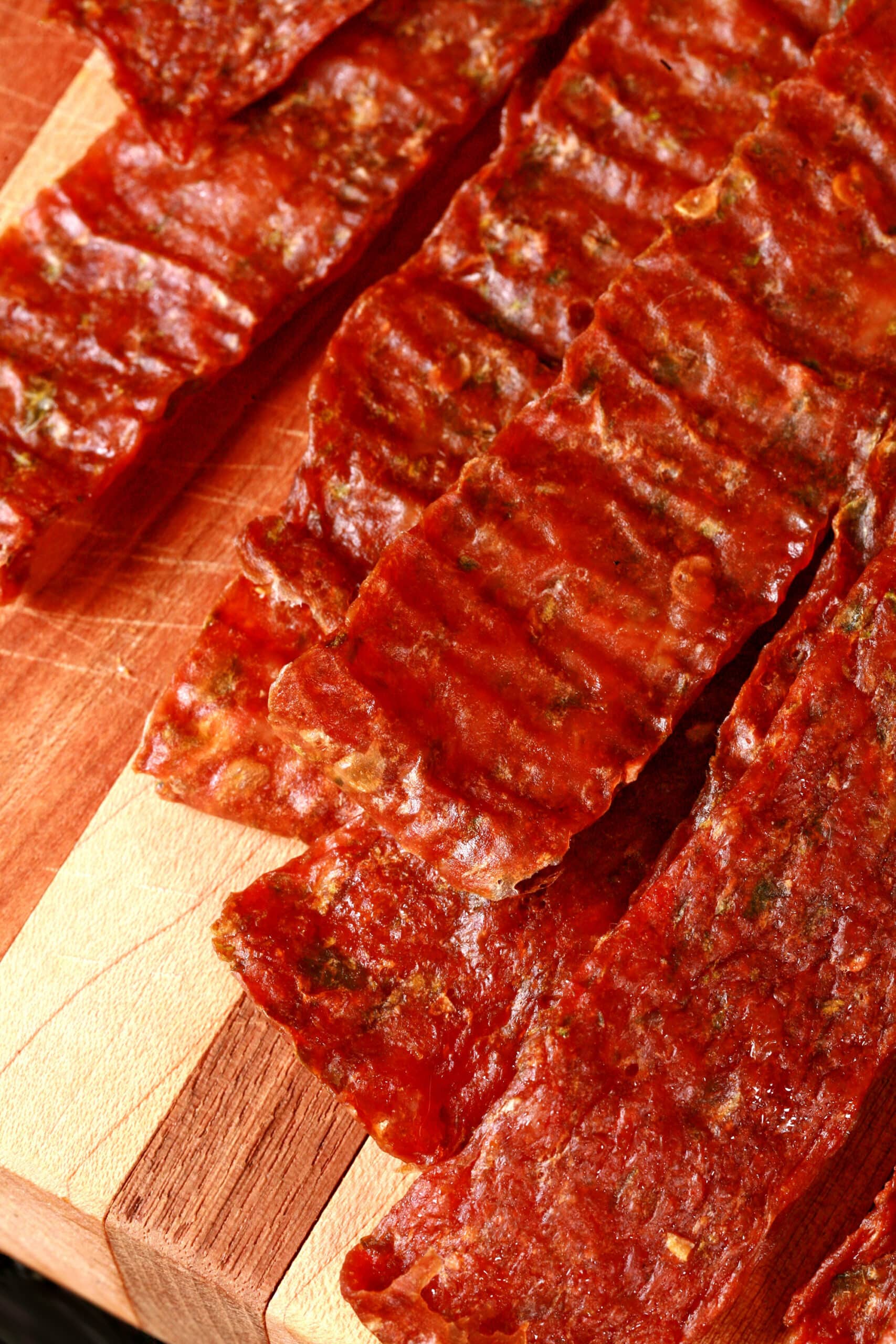 A pile of homemade jalapeno chicken jerky on a wooden cutting board, along with 2 jalapenos.