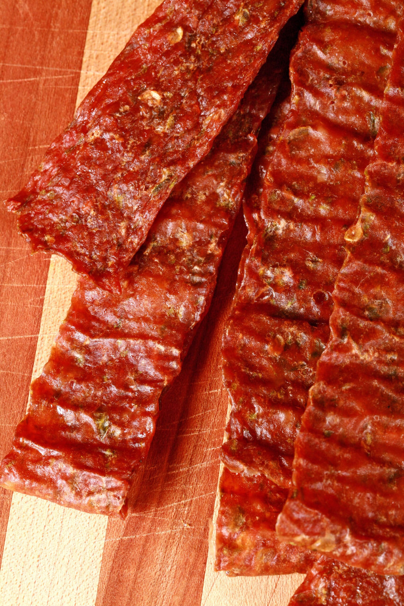 A pile of homemade jalapeno chicken jerky on a wooden cutting board, along with 2 jalapenos.