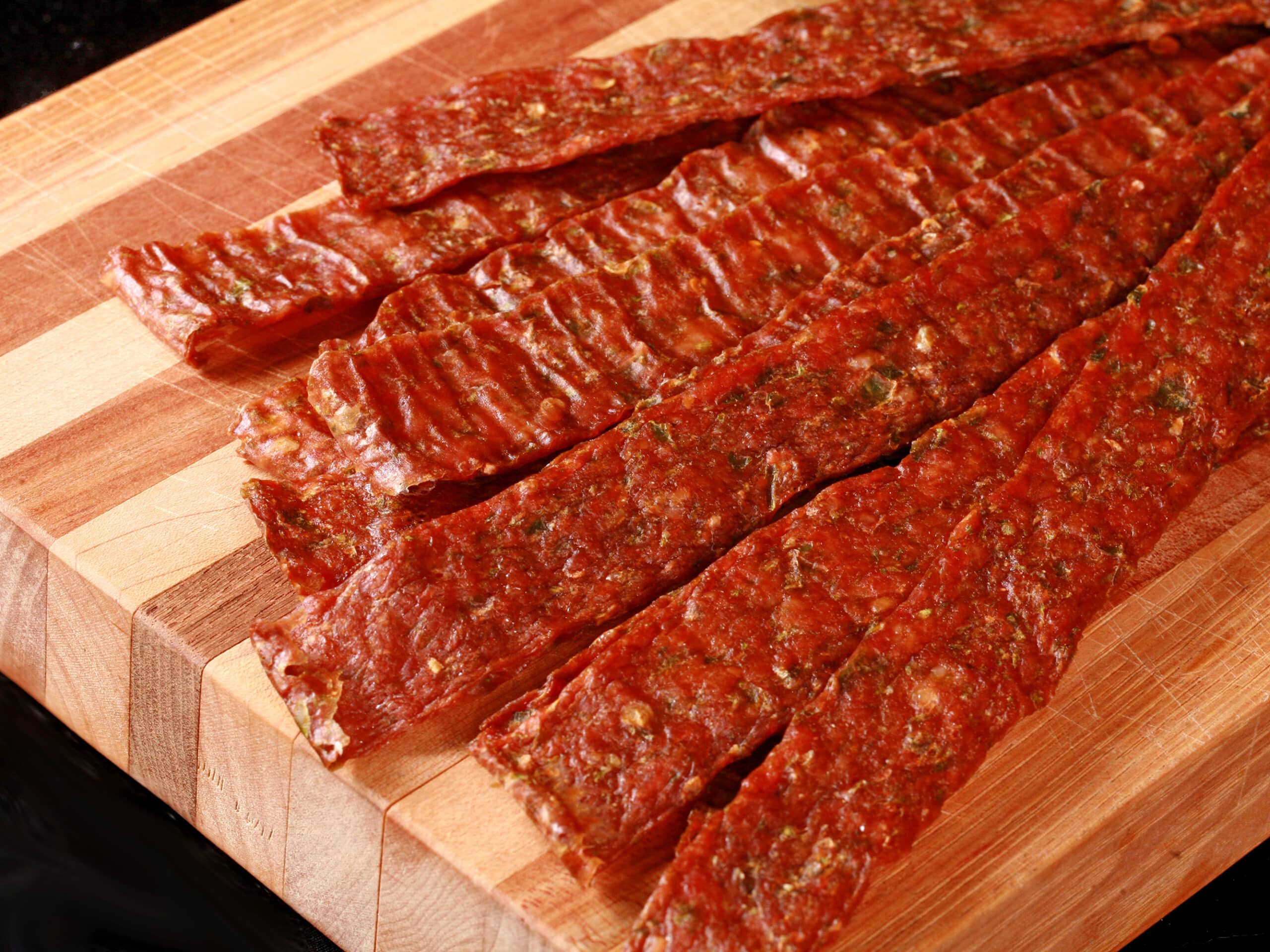 A pile of homemade chicken jerky on a wooden cutting board, along with 2 jalapenos.