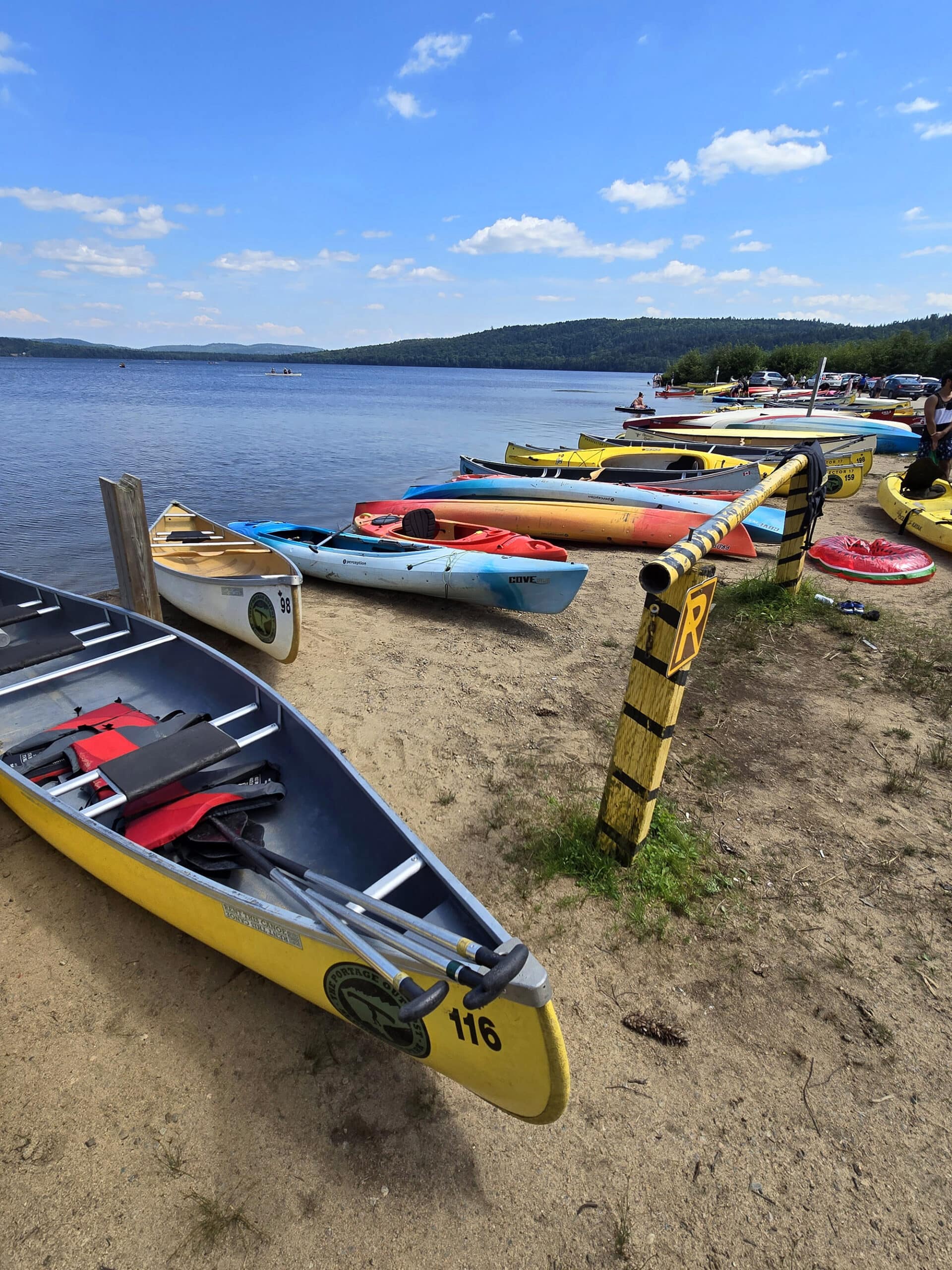 A row of brightly coloured canoes and kayaks on the sandy beach at Lake of Two Rivers Campground.