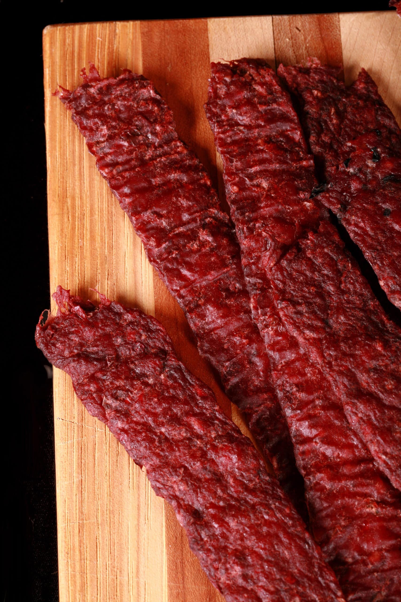 Several strips of homemade elk jerky on a wooden cutting board, along with a small bowl of lingonberries.