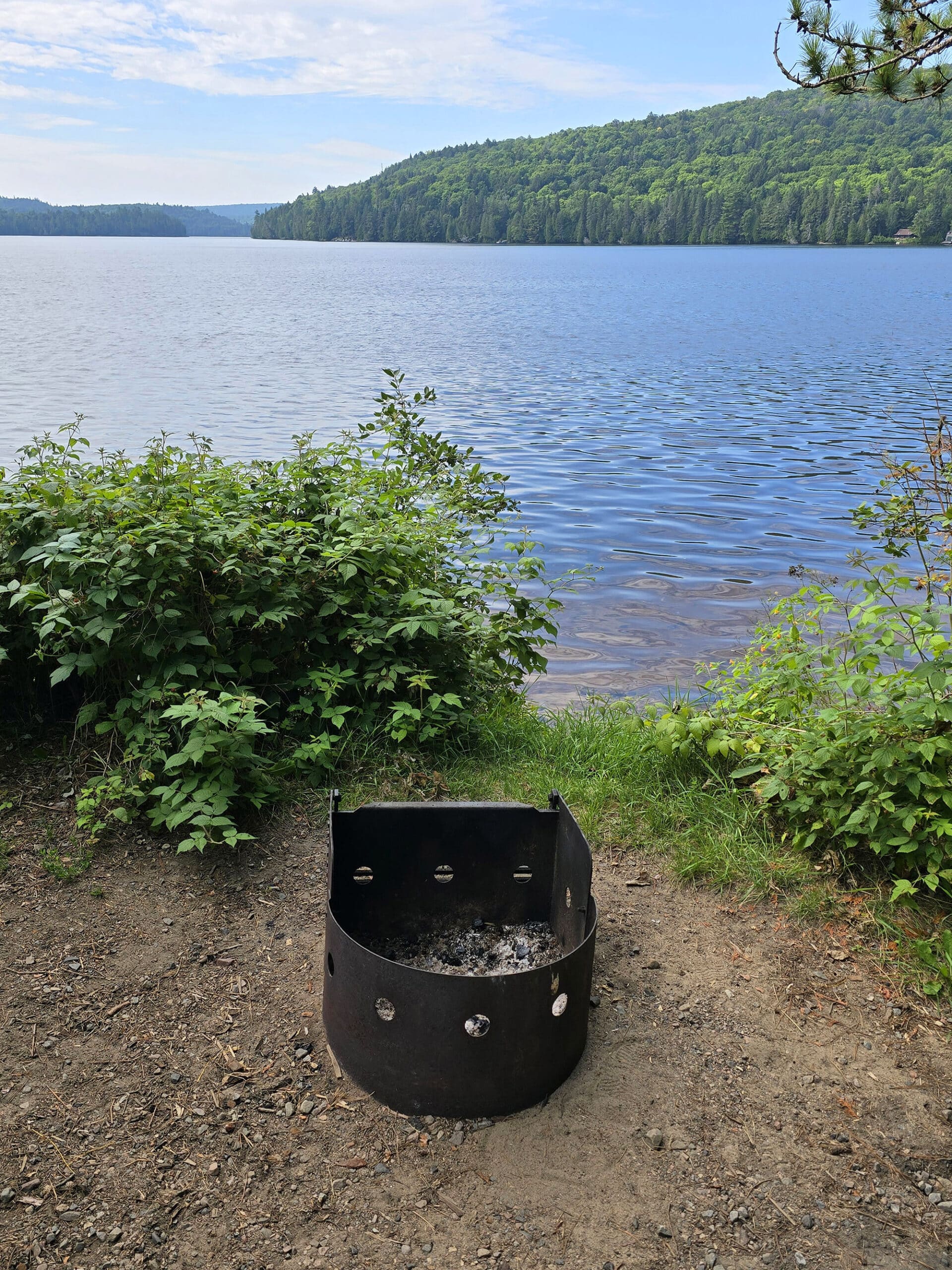 A campsite overlooking rock lake, with a firepit in the foreground.