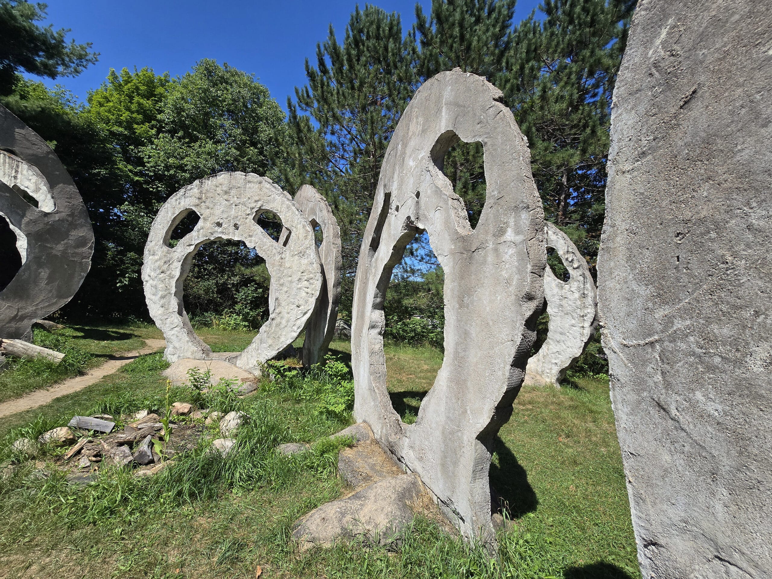 A grassy area with several 18 foot tall concrete sculptures that look like screaming heads.