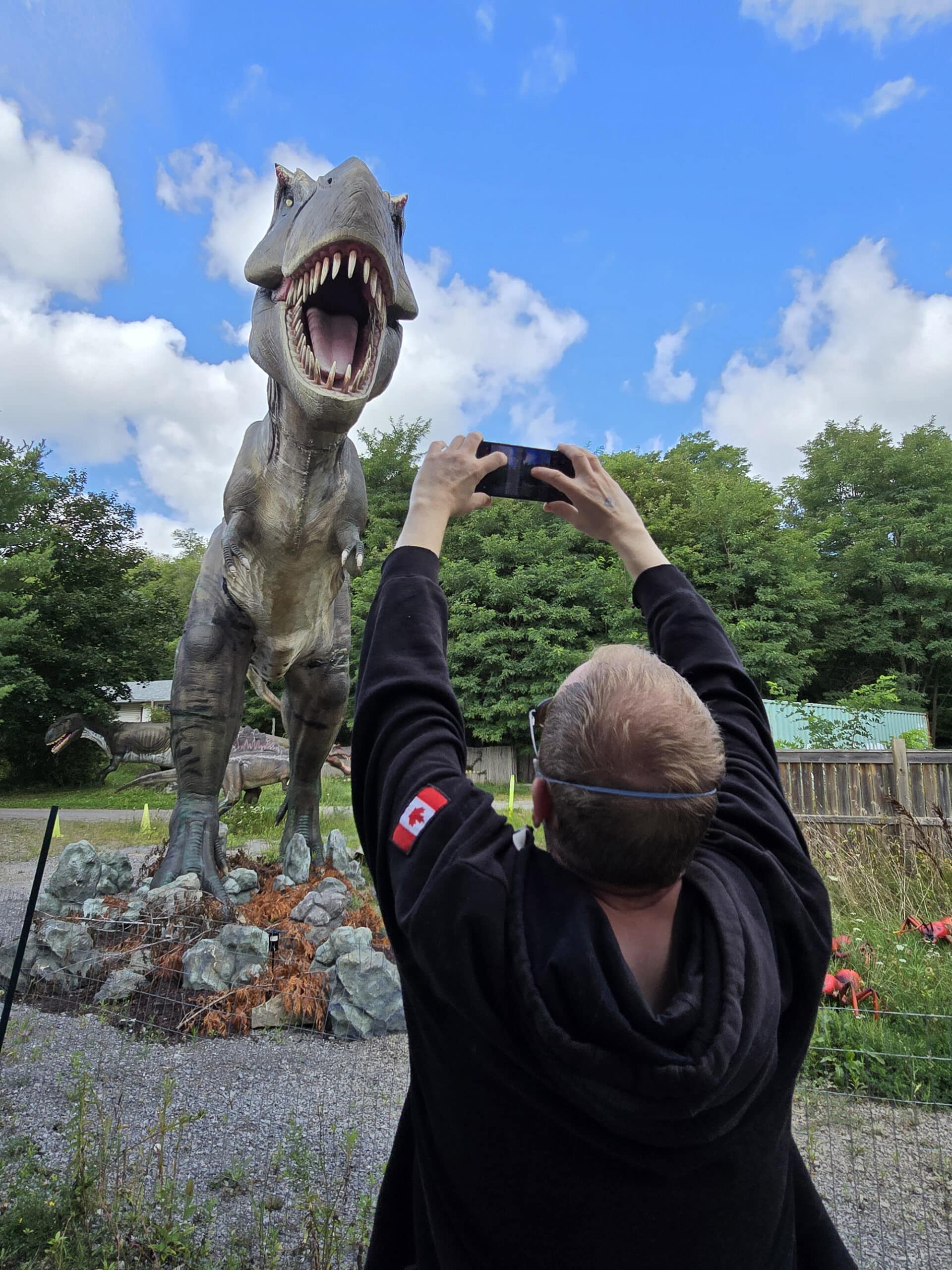 A middle aged white man taking a photo of a life sized tyrannosaurus rex.