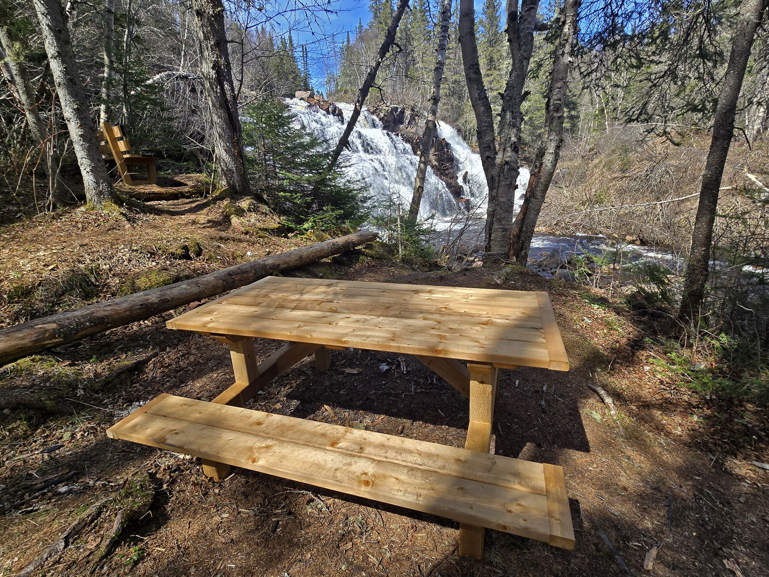 A picnic table and a bench in the distance, both overlooking mink creek falls.
