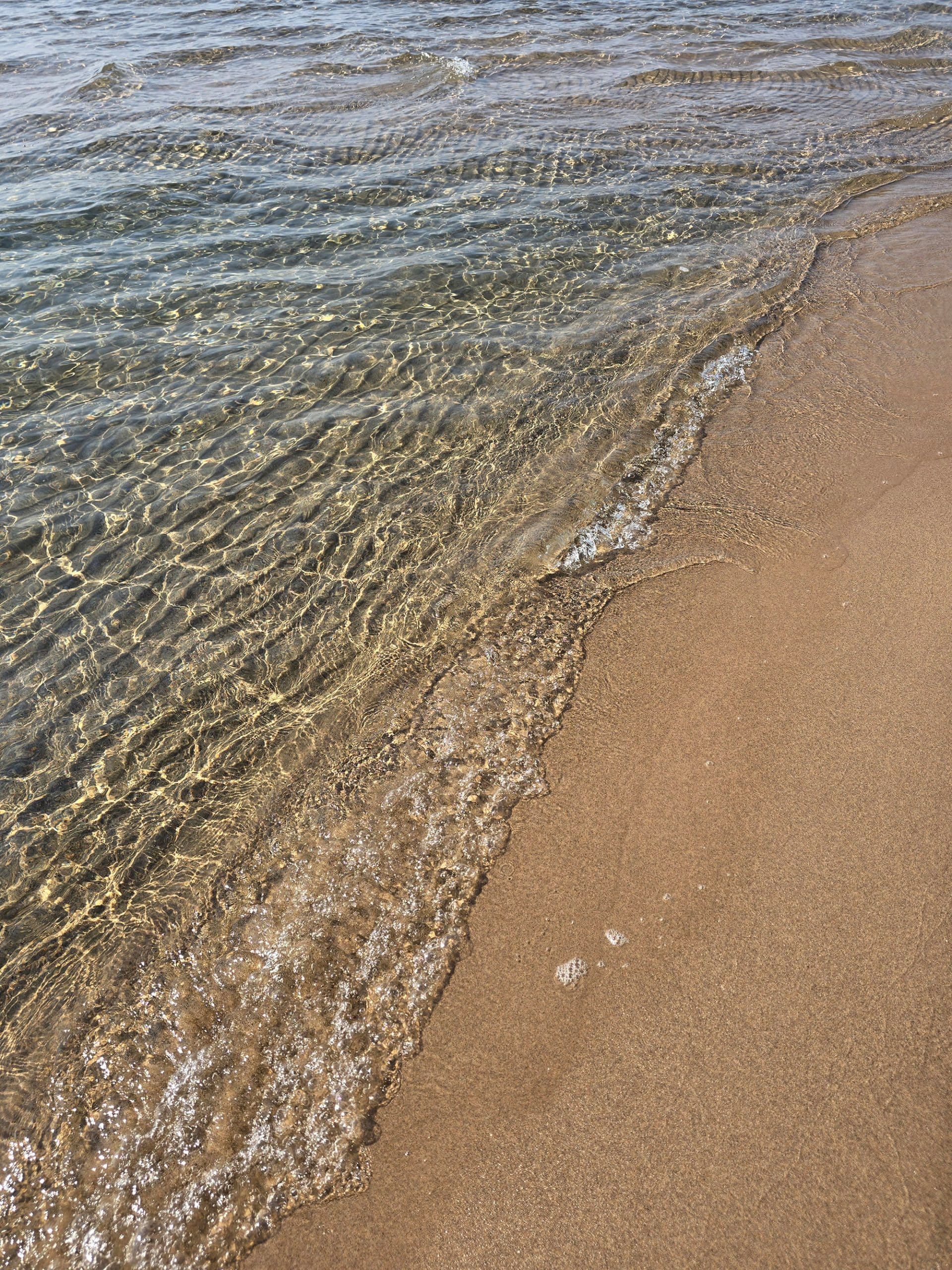 Ripples of clear lake superior water on a sandy beach.