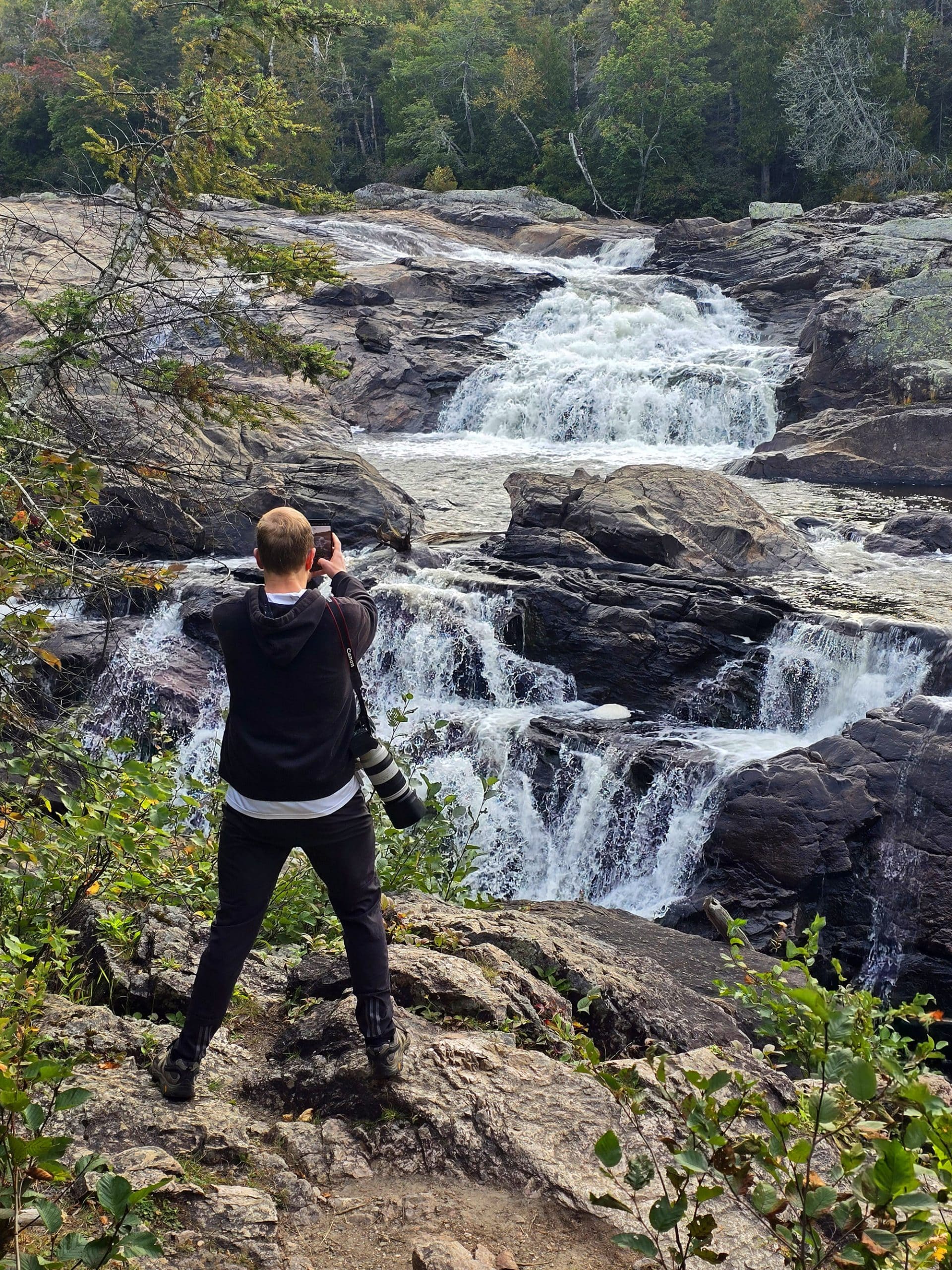 A middle aged man photographing one of the waterfalls at Sand River Falls on the Pinguisibi Trail.