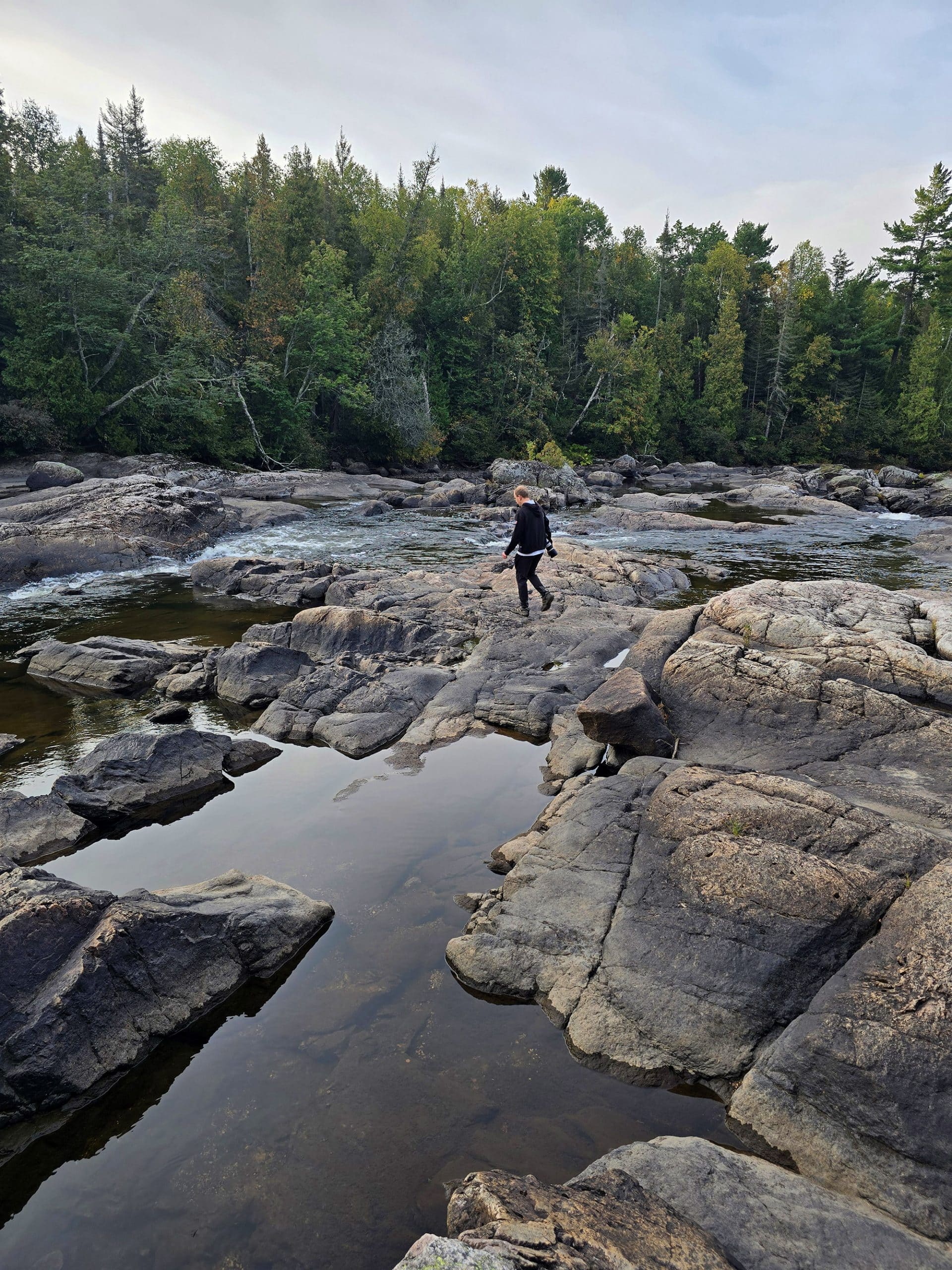 A middle aged pan walking out onto the rocks at one of the waterfalls at Sand River Falls on the Pinguisibi Trail.