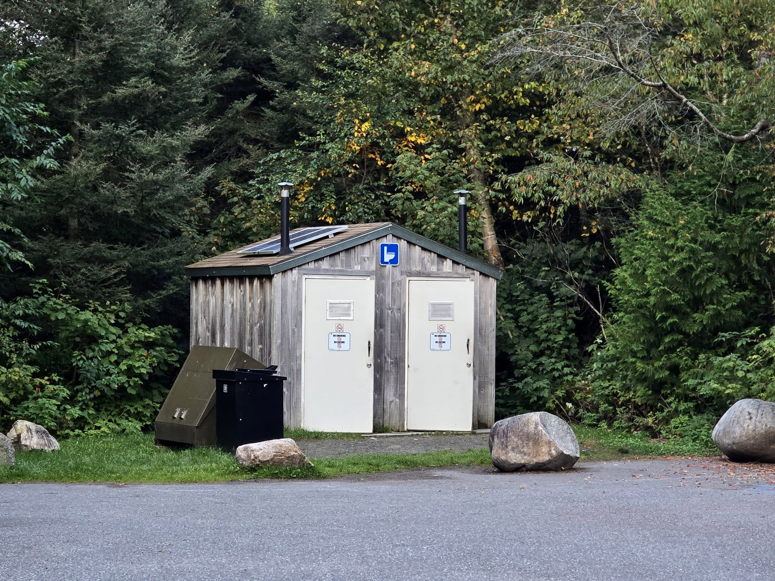 A 2 stall outhouse on the side of the sand river falls parking lot.