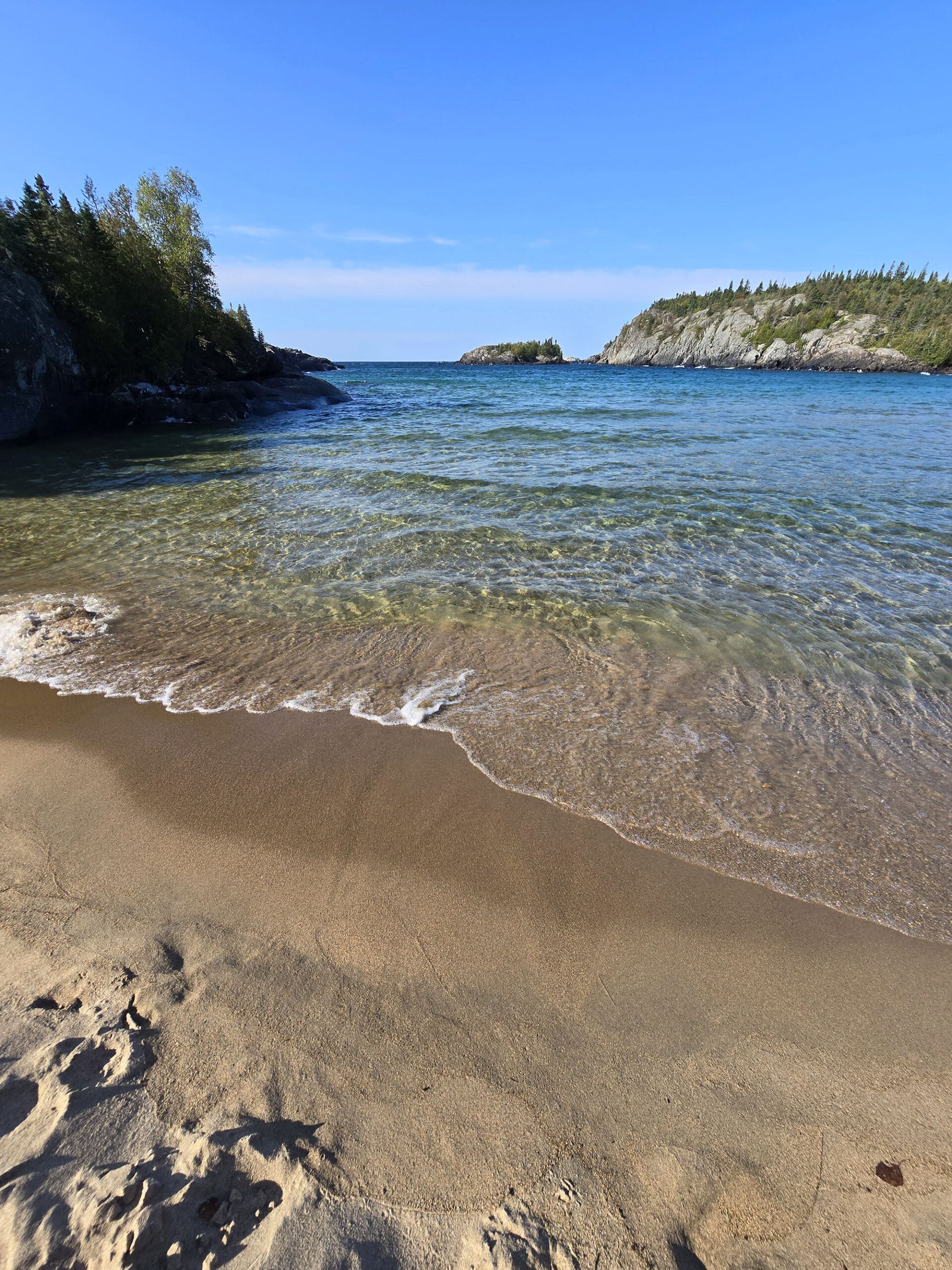 A sandy beach on lake superior, with clear water.