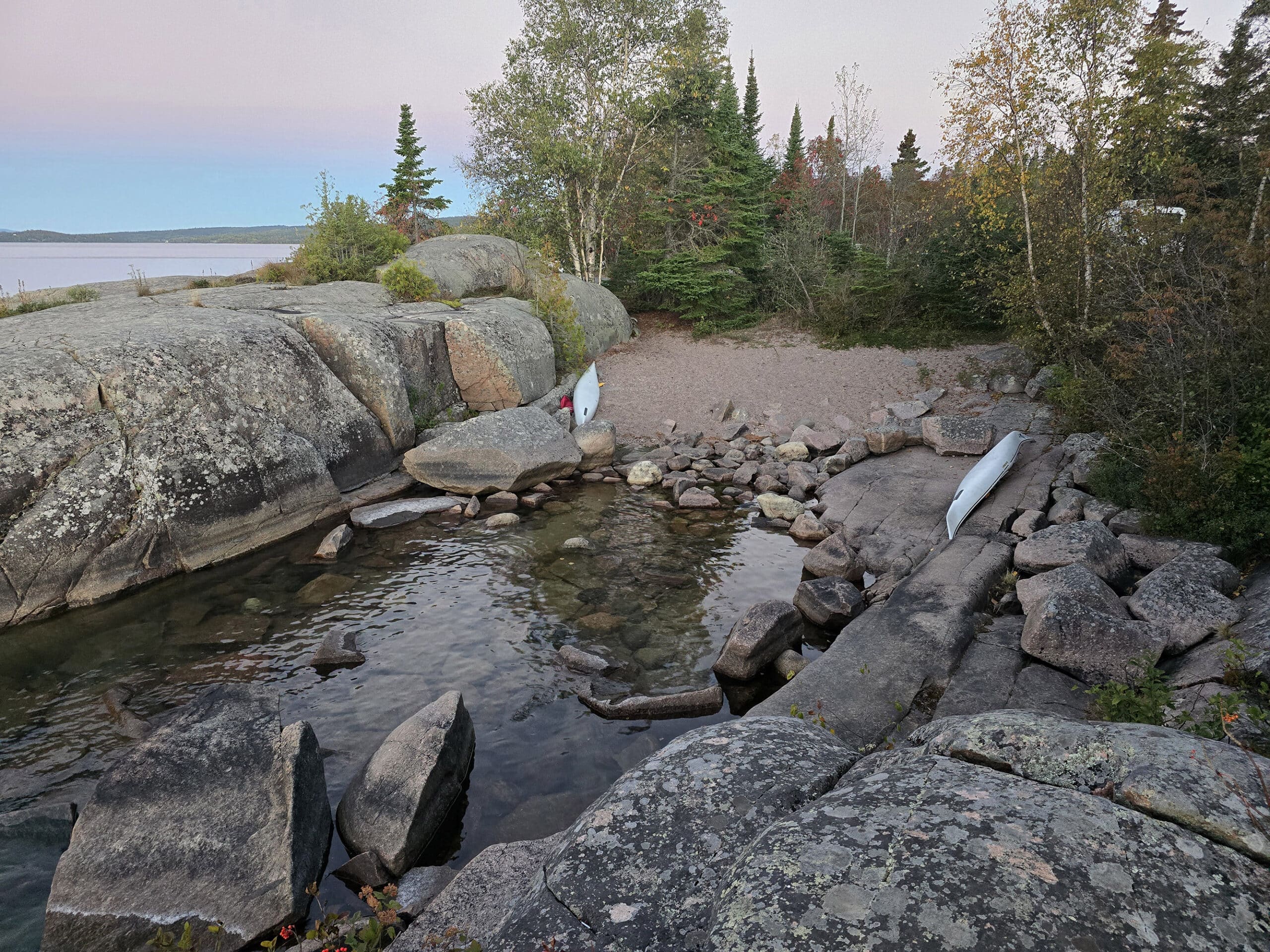 A rocky inlet with a sandy beach and campsite behind it.