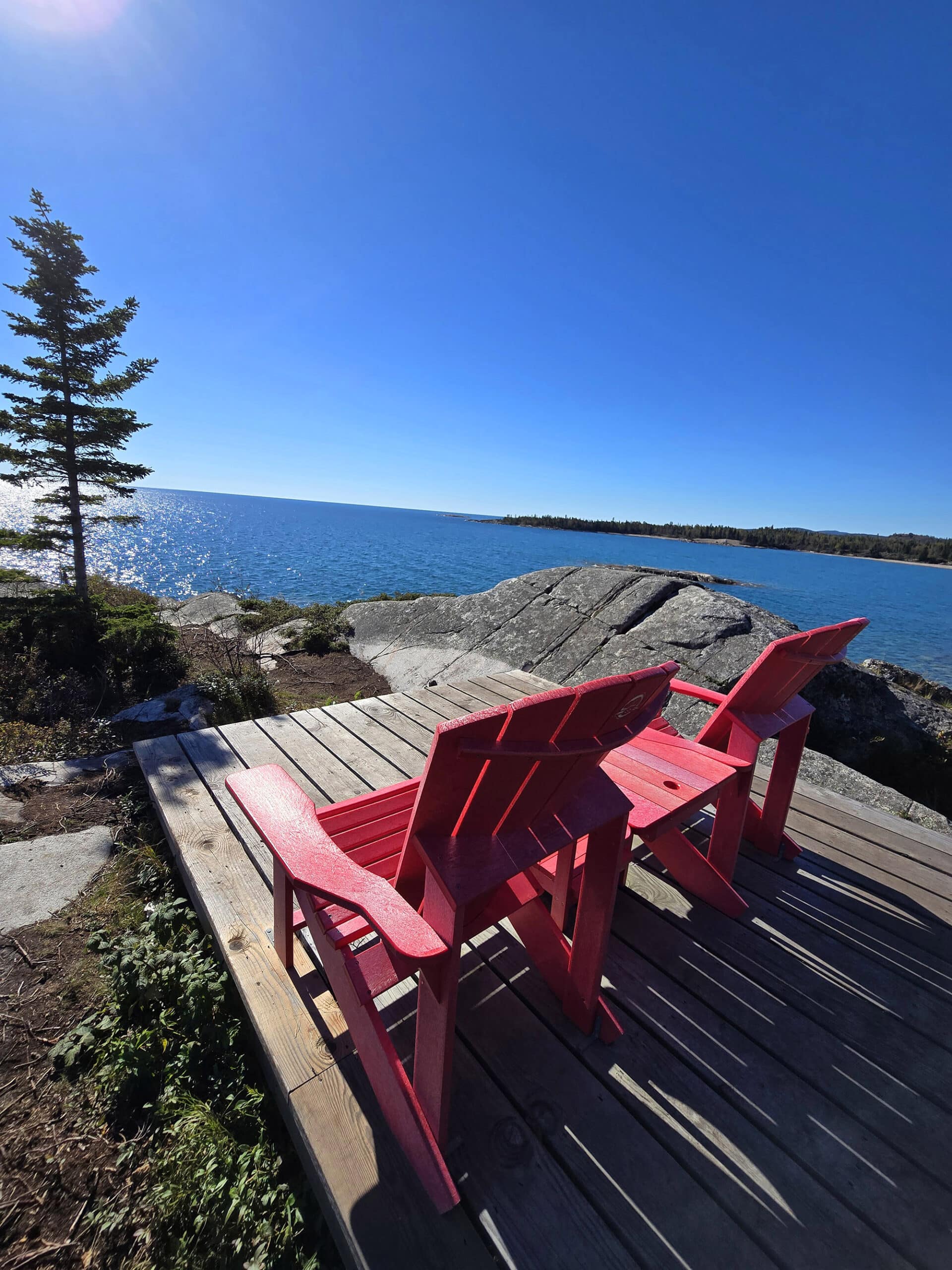 2 red chairs on a deck overlooking terrace bay beach and lake superior.