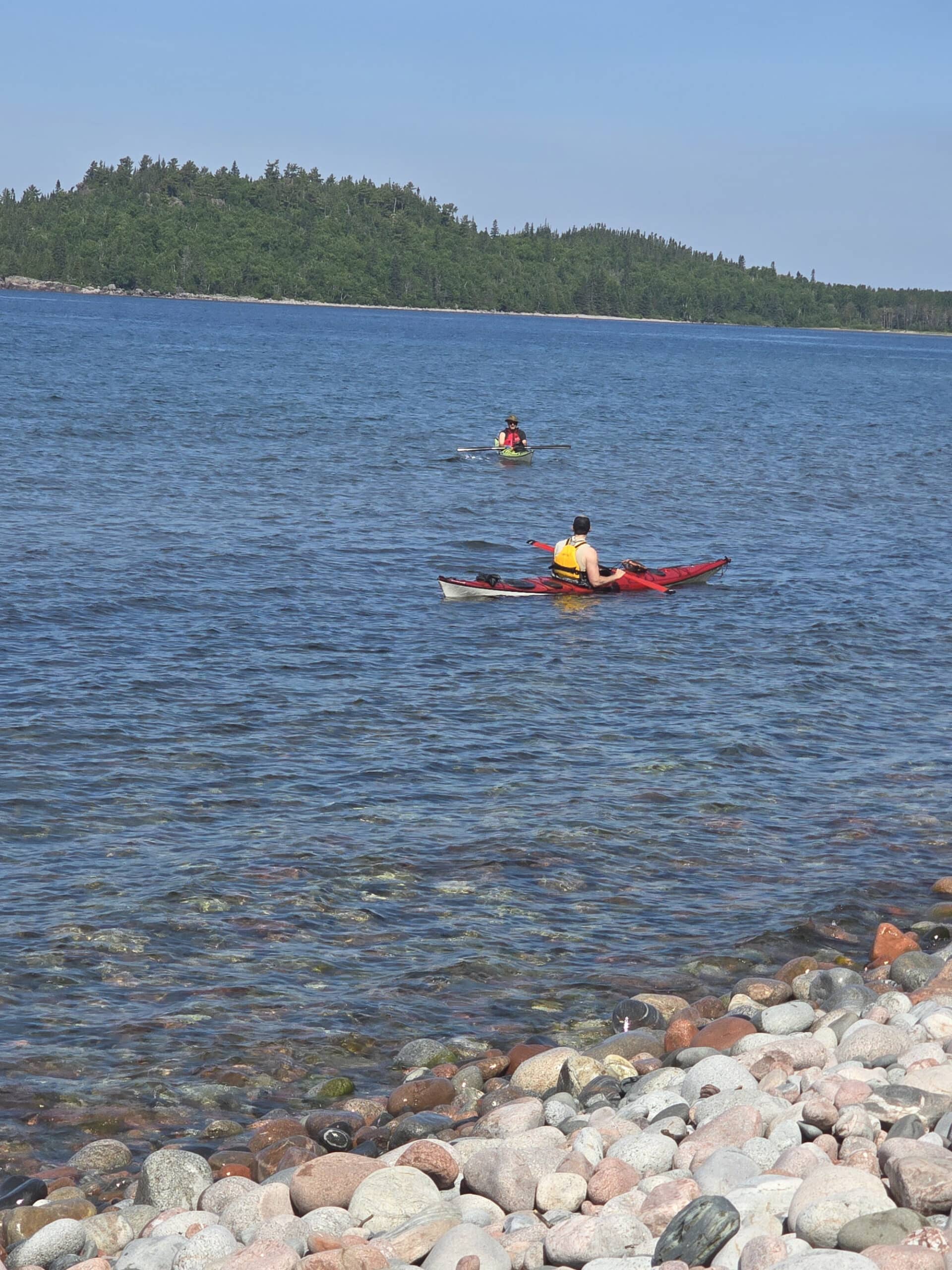 2 people kayaking on Lake Superior, with a rocky beach in the foreground.