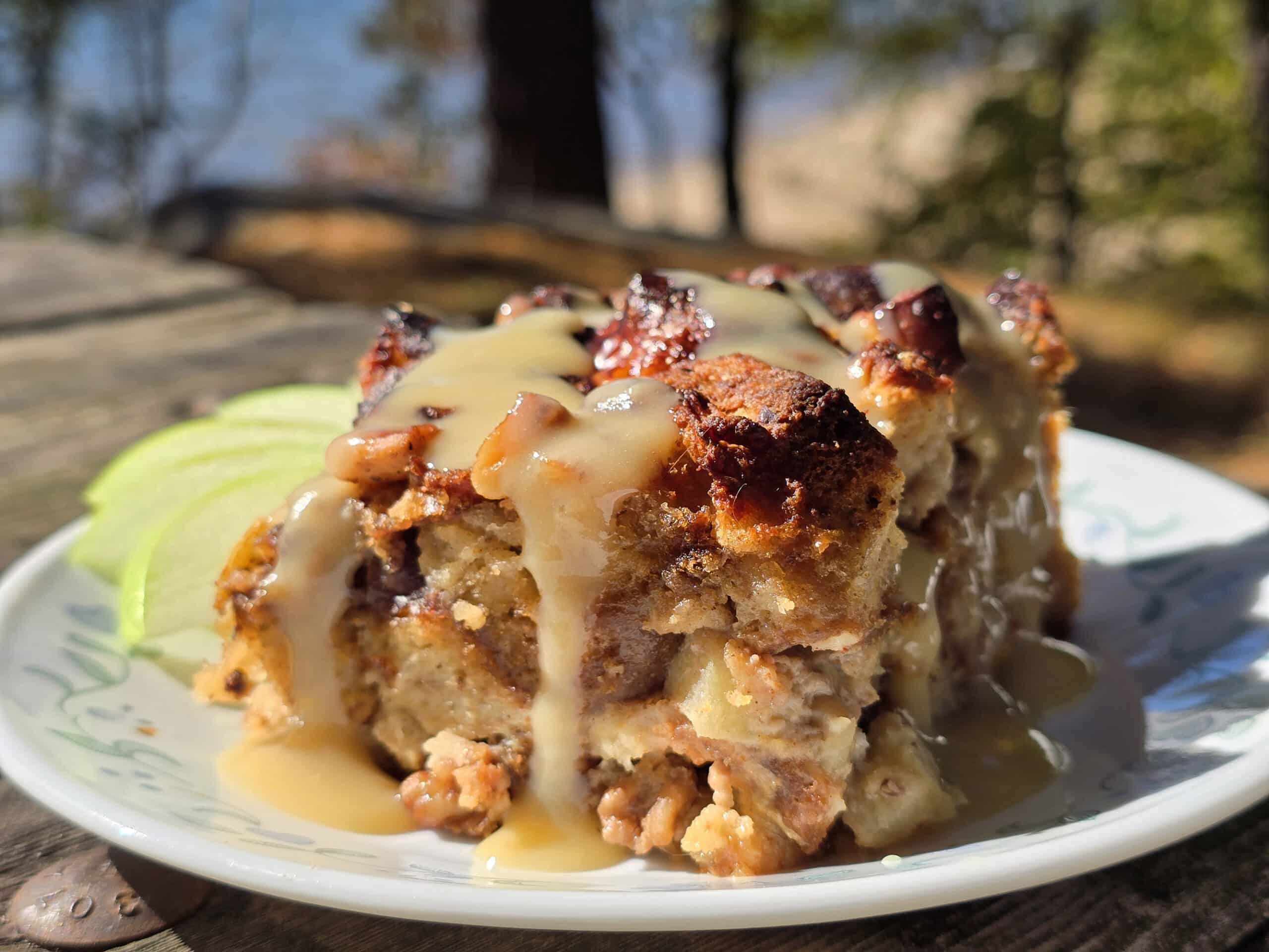 A plate of bread pudding made from apple fritters, drizzled with homemade maple cream sauce.