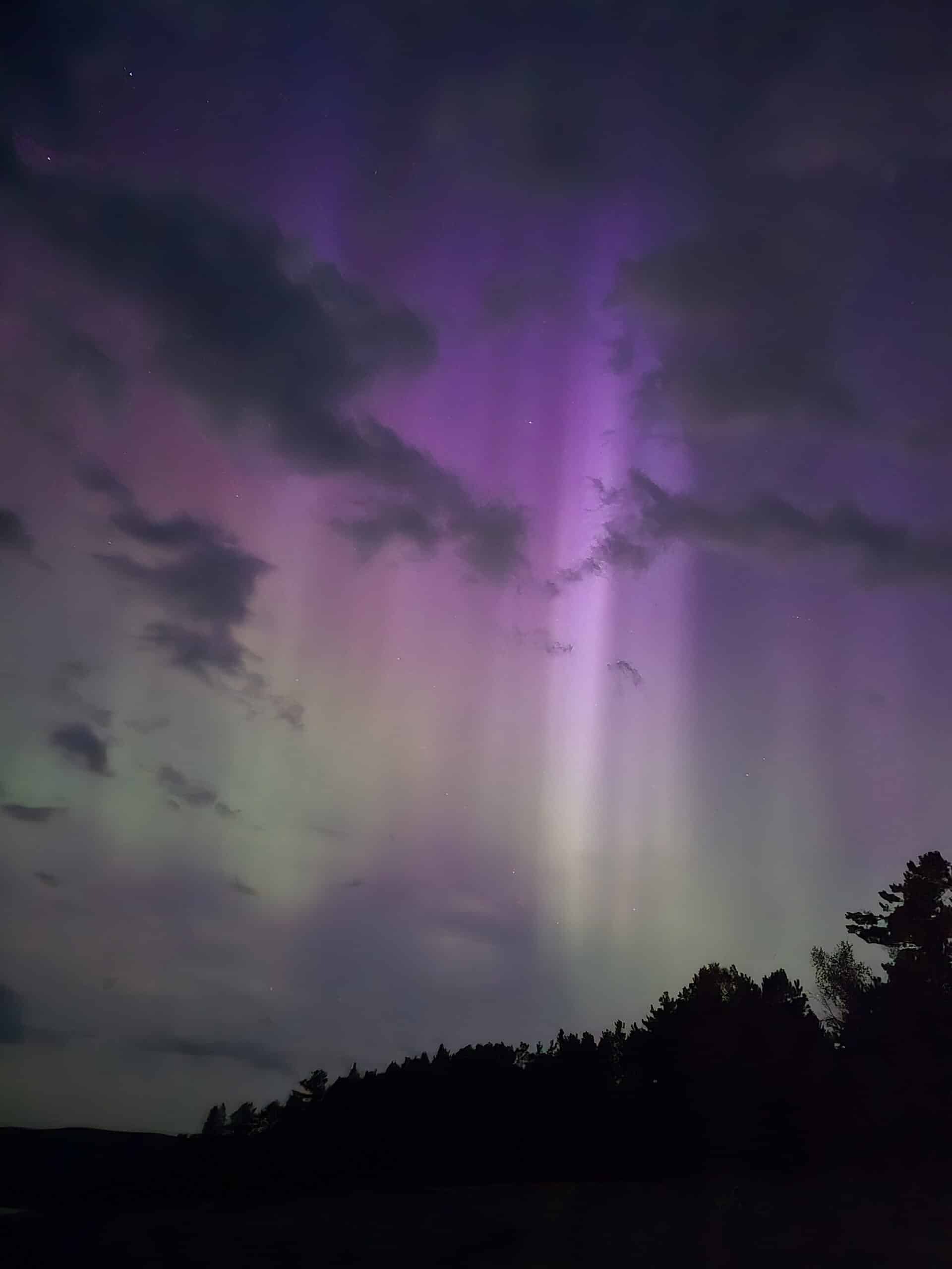 A bright pink, purple, and green northern lights display over lake superior.