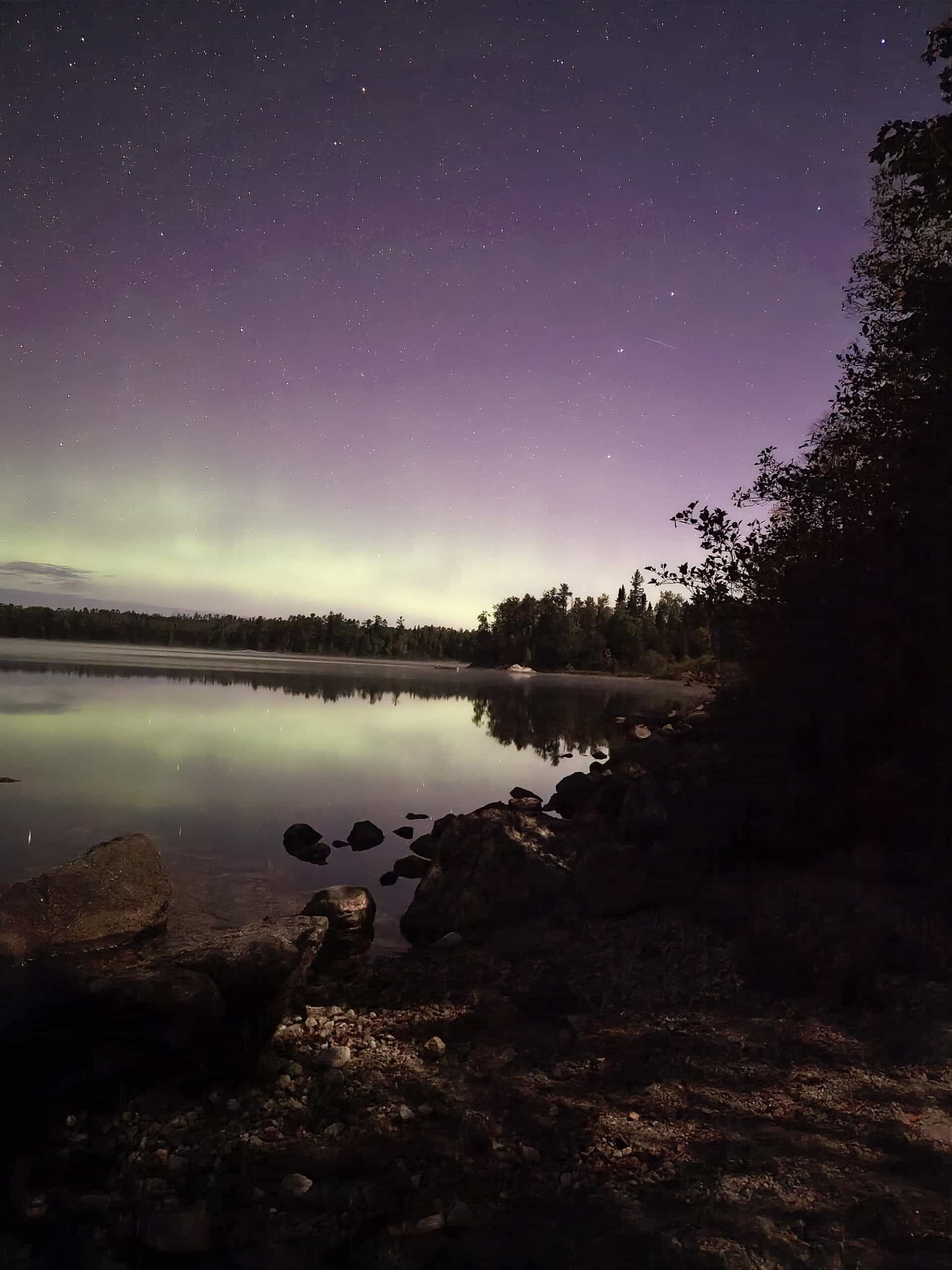 A bright purple and green northern lights display over a lake.