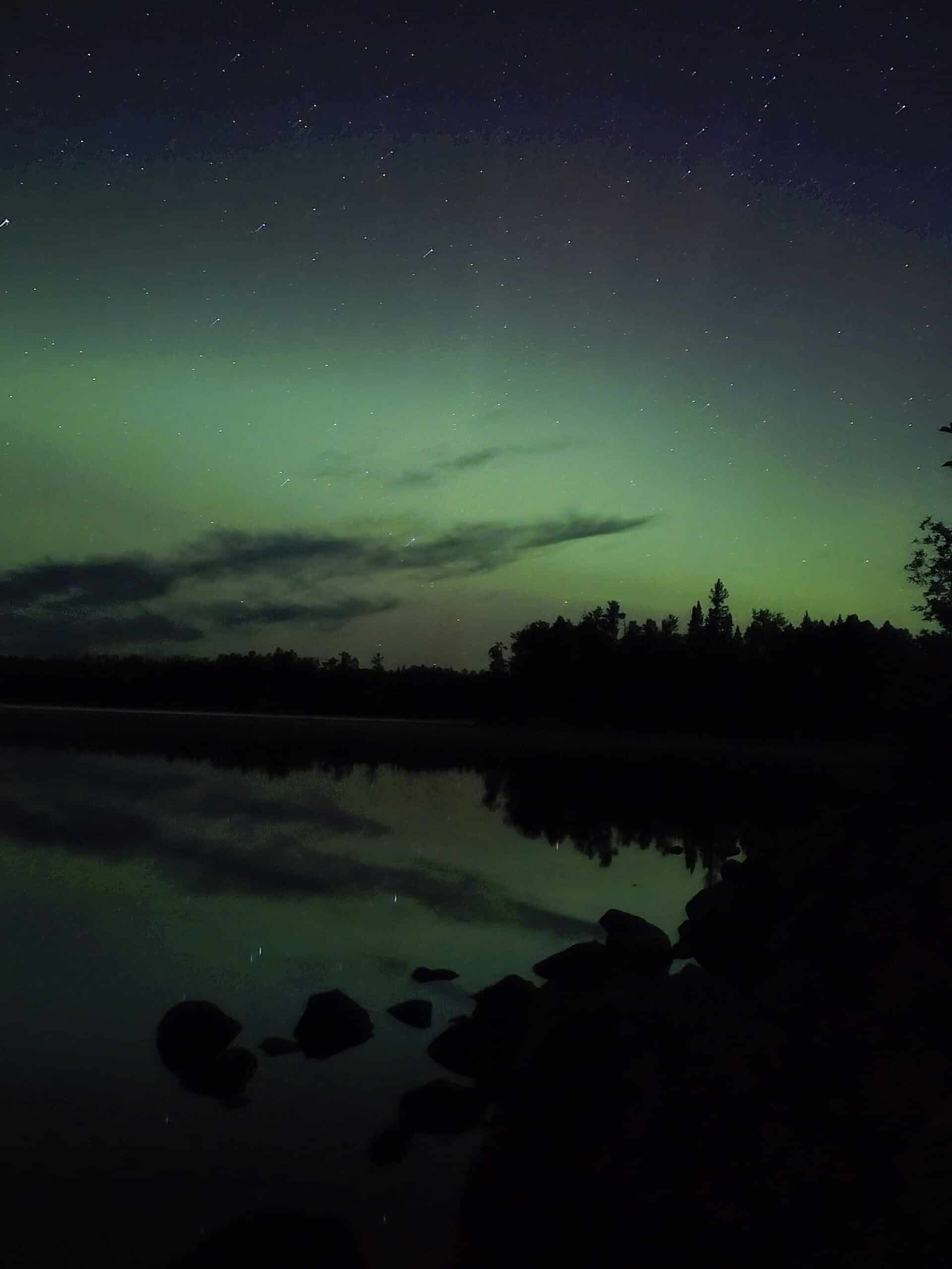 A bright blue and green northern lights display over a lake.