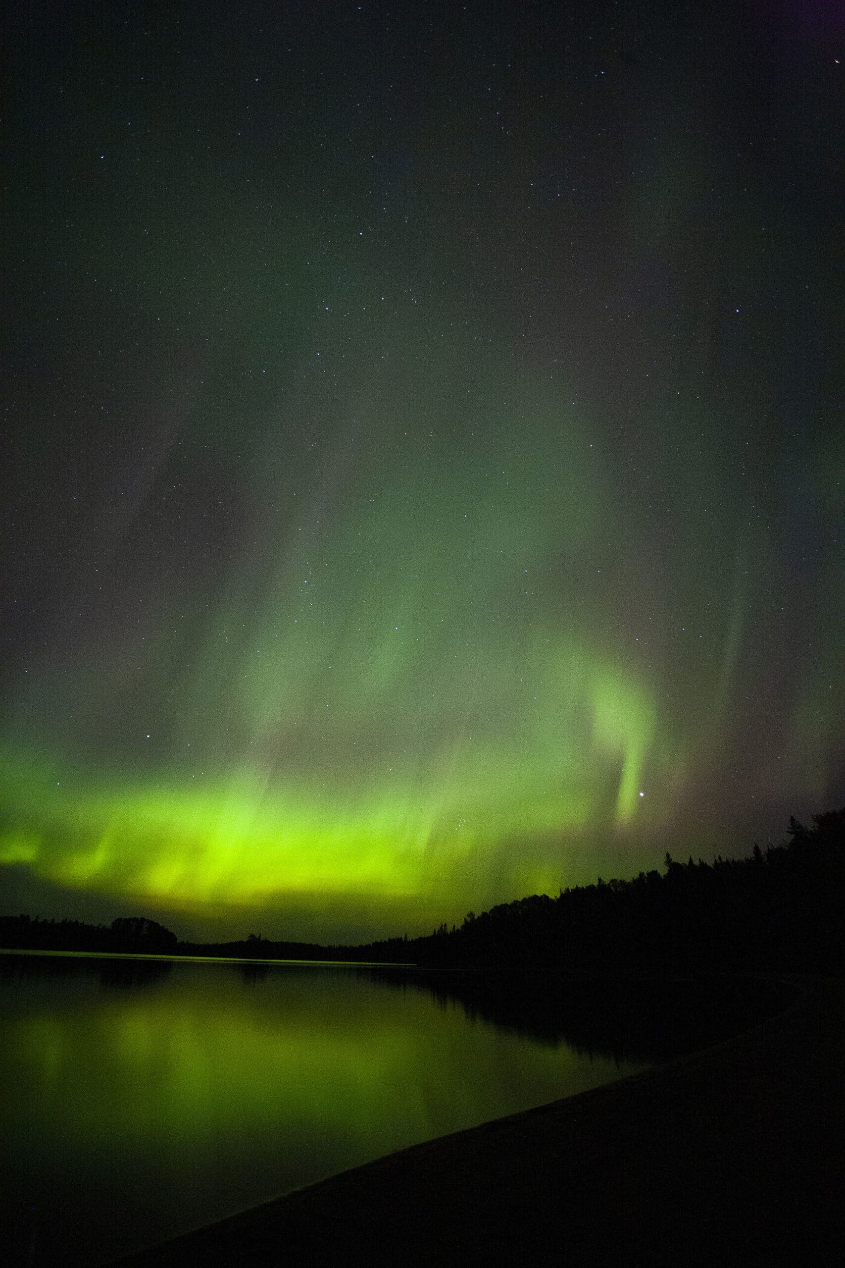 A bright green northern lights display over a lake.