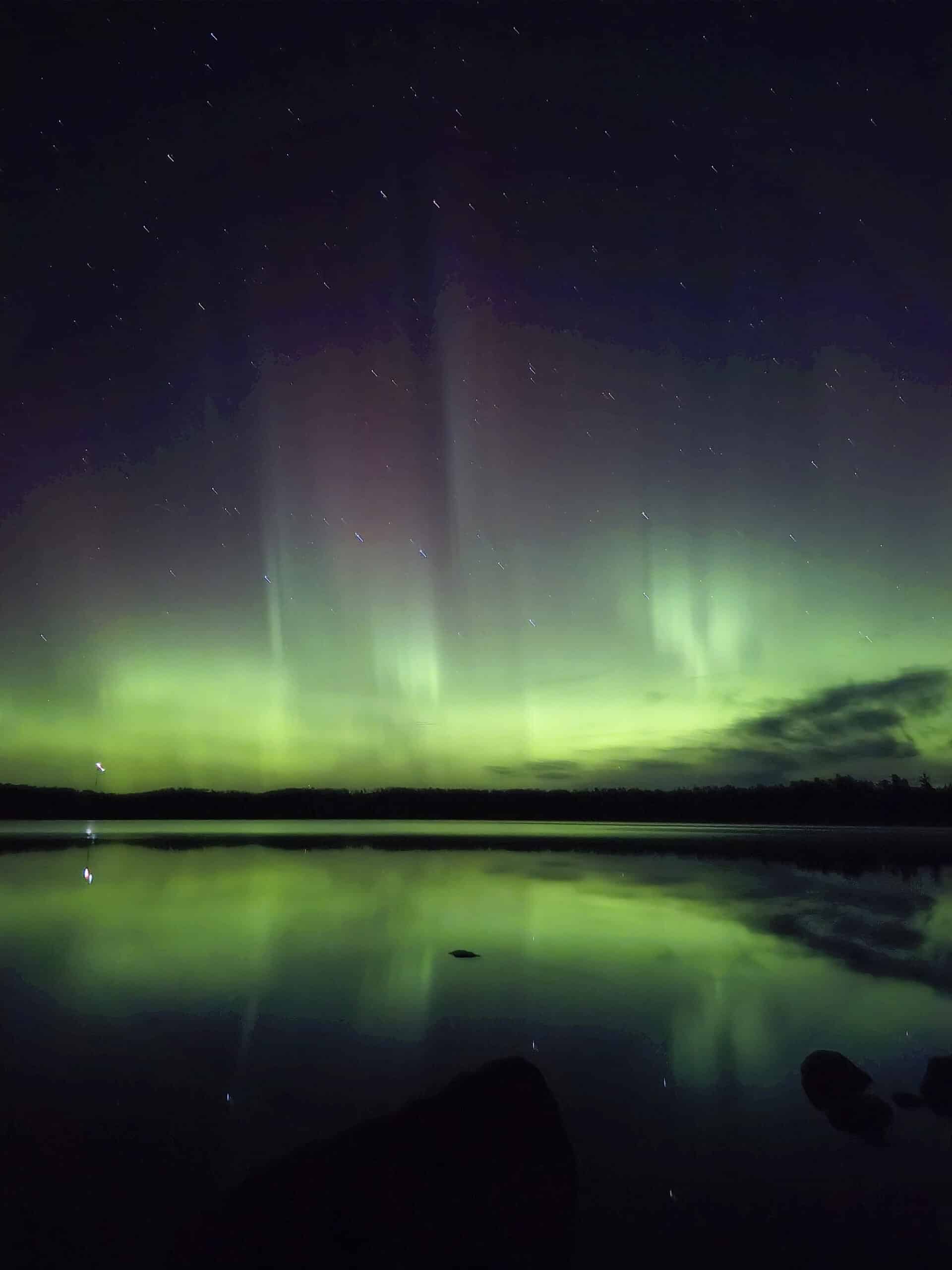 A bright purple and green aurora borealis display over a lake.