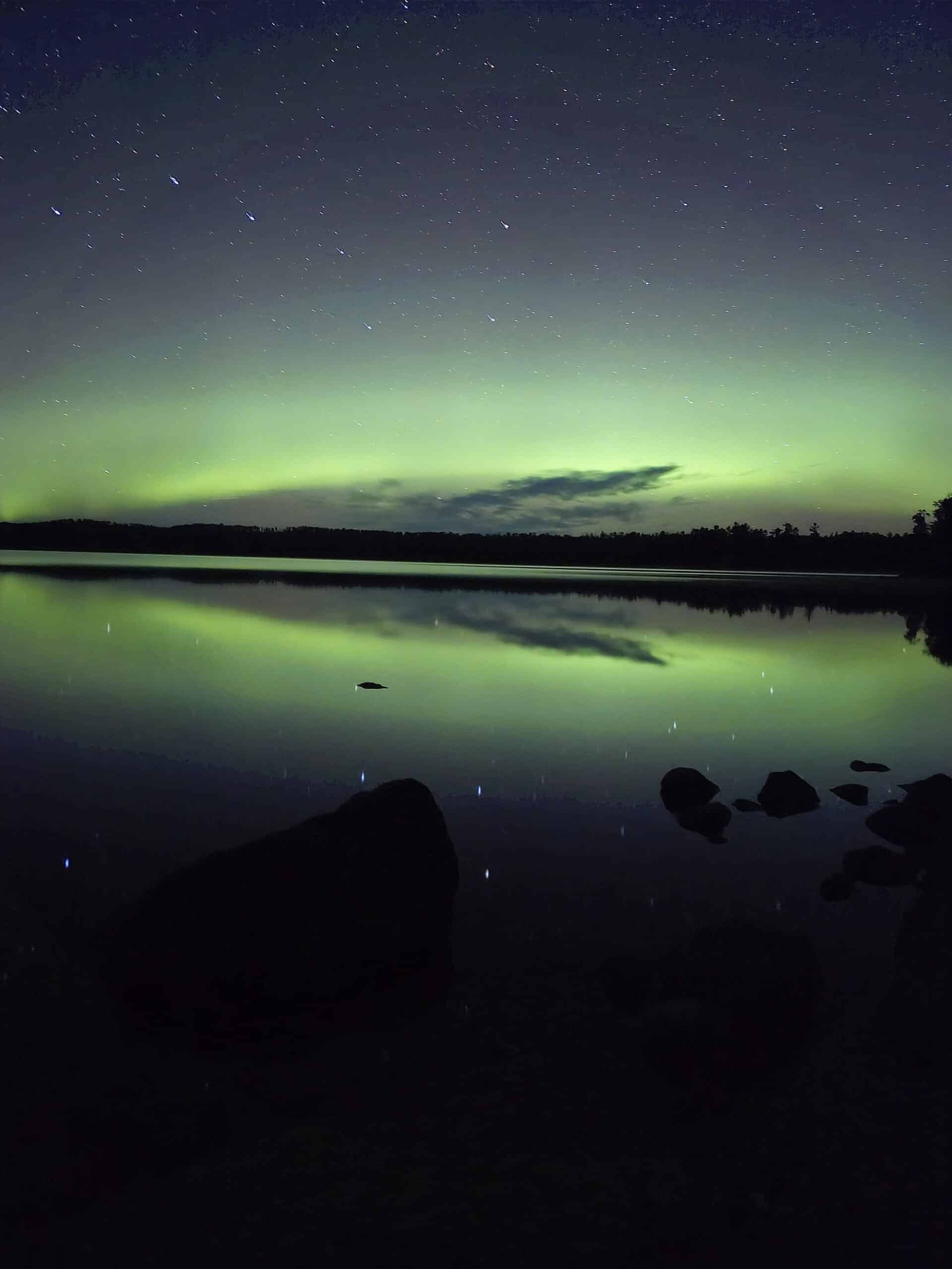 A bright blue and green aurora borealis display over a lake.