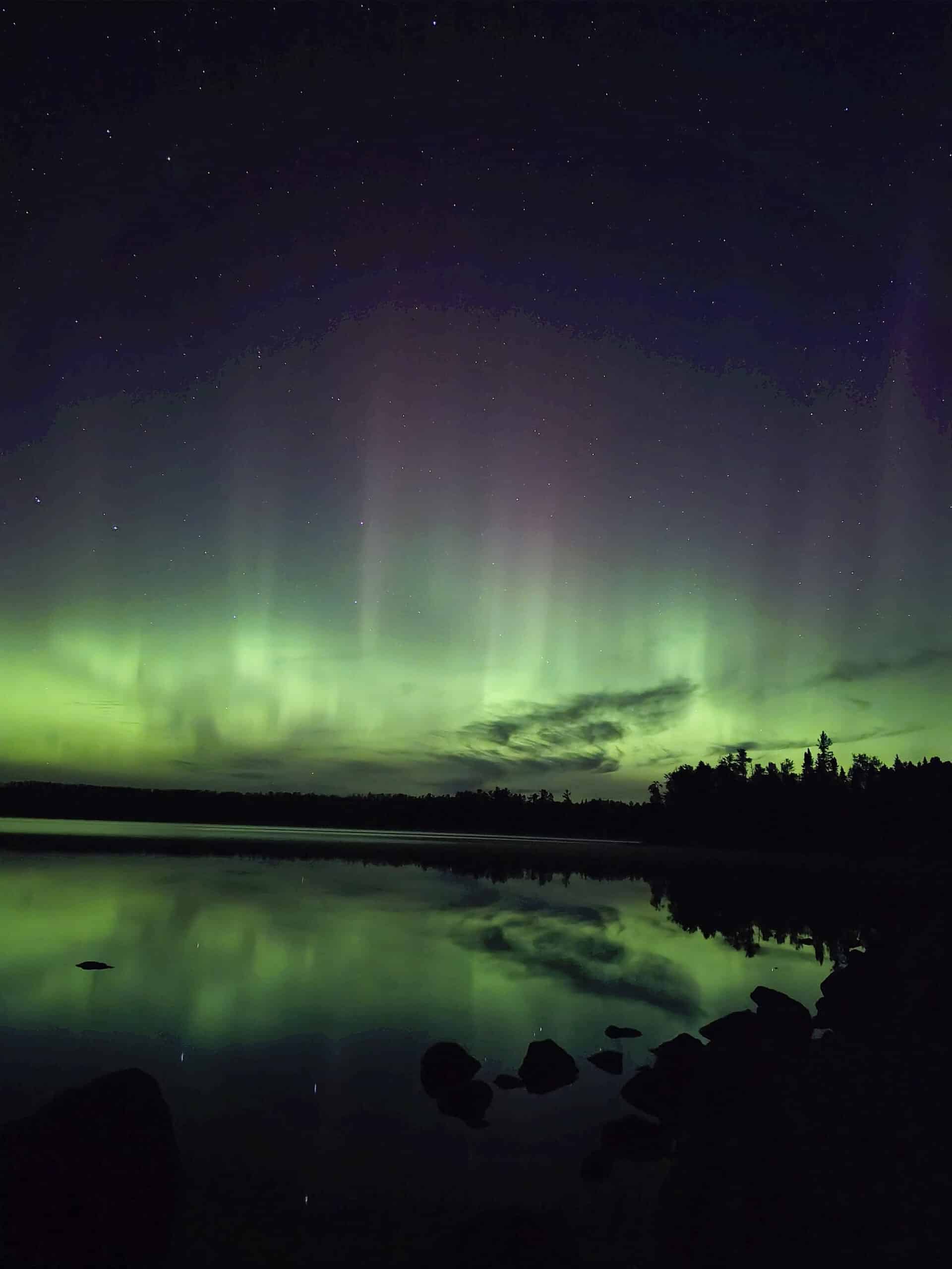 A bright blue and green northern lights display over a lake.