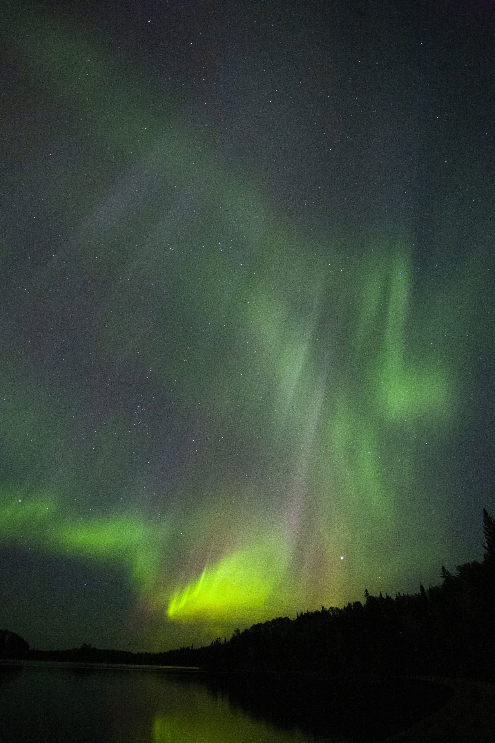 A bright purple and green aurora borealis display over a lake.