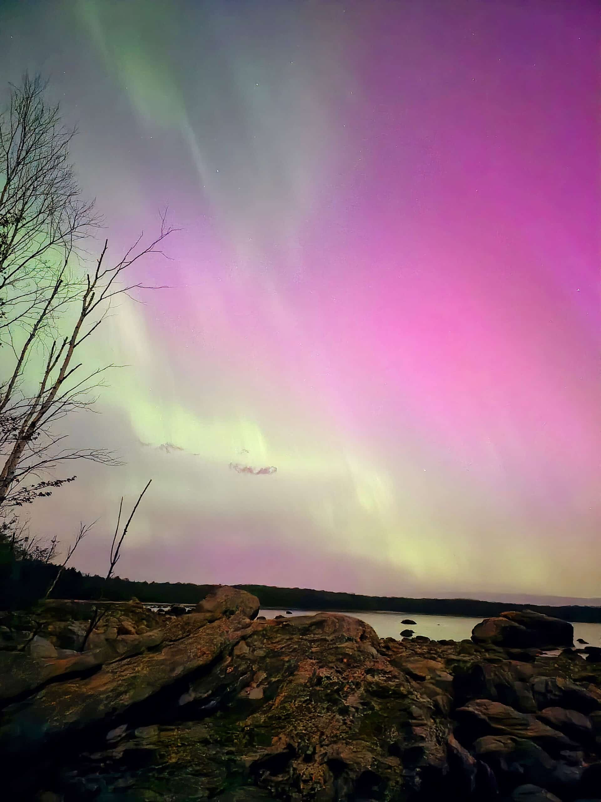 A bright pink and green northern lights display over lake huron.