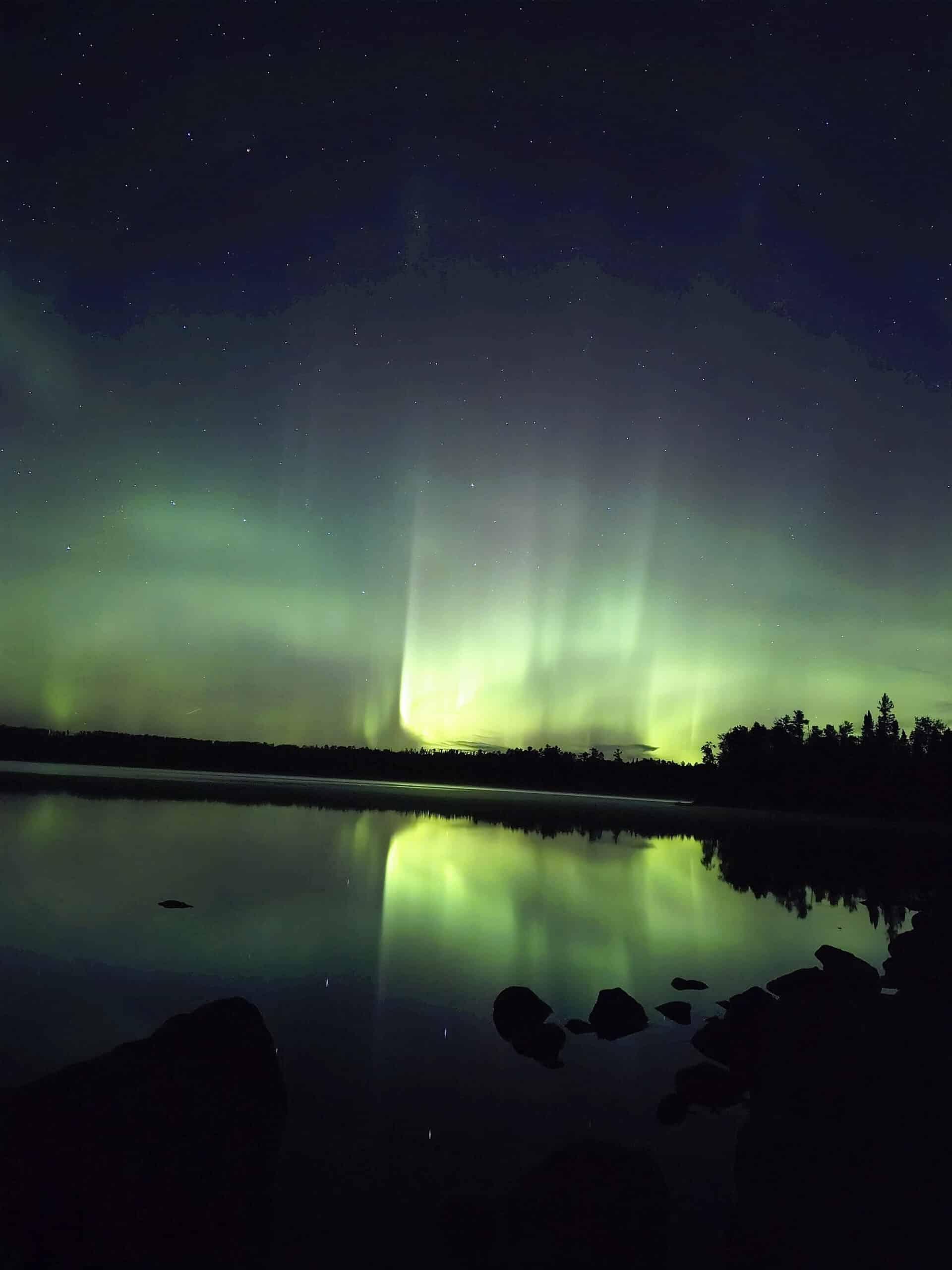 A bright purple, blue, and green aurora borealis display over a lake.