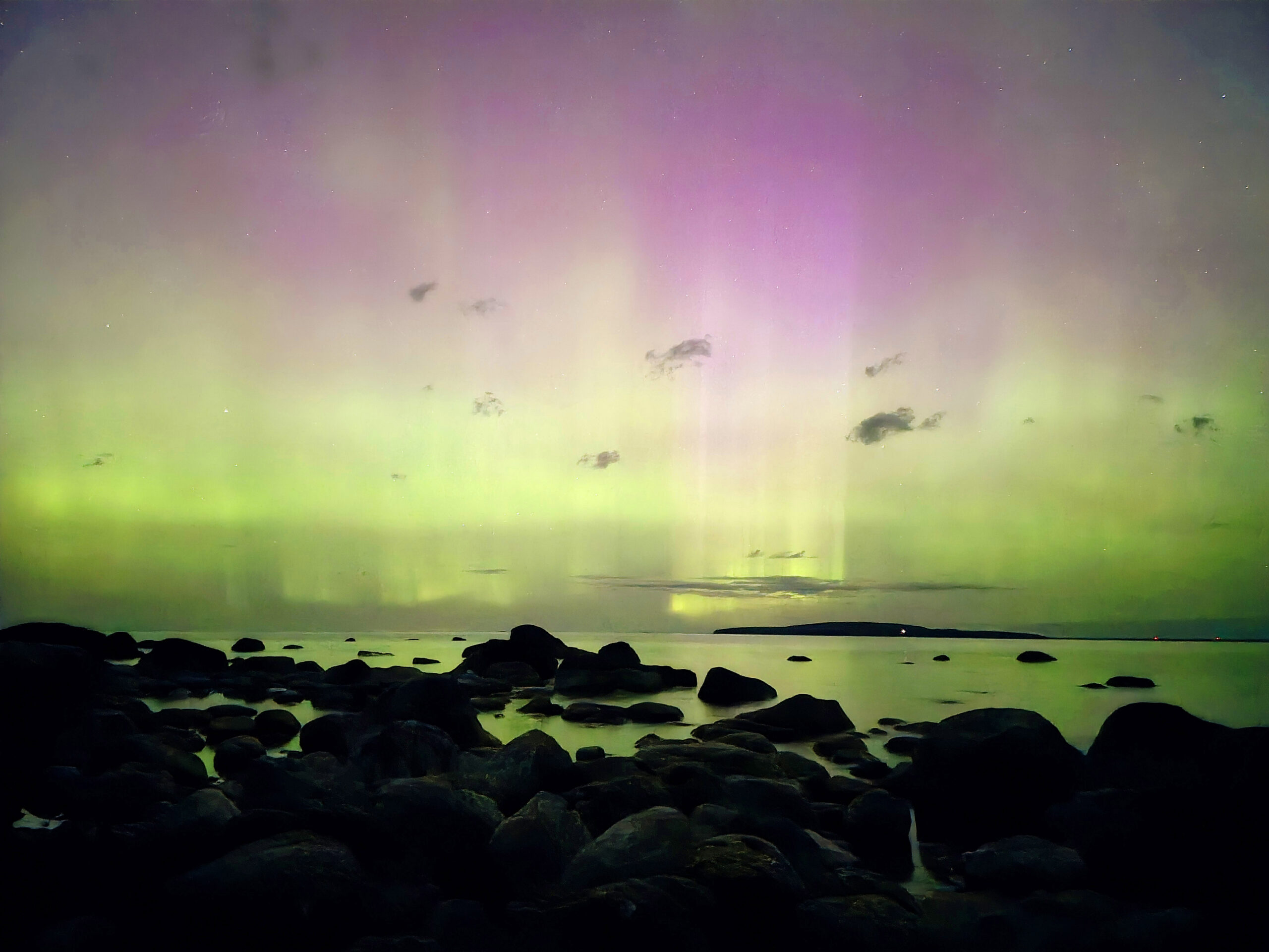 A bright pink and green aurora borealis display over a georgian bay.