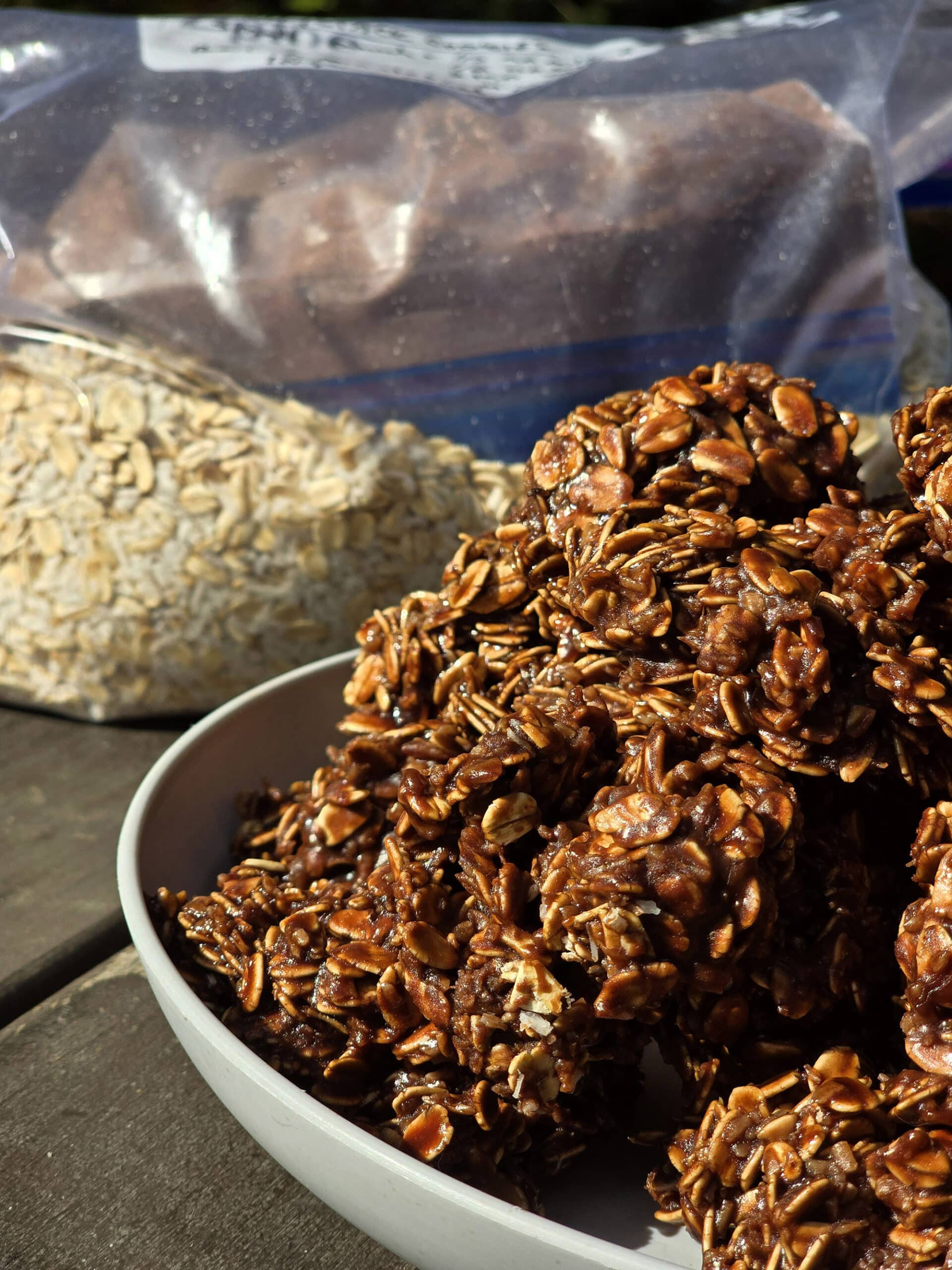 A plate of campfire chocolate haystack cookies on a picnic table, in front of a bag of homemade cookie mix.