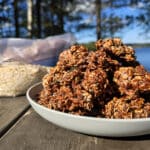 A plate of campfire chocolate haystack cookies on a picnic table, in front of a bag of homemade cookie mix.