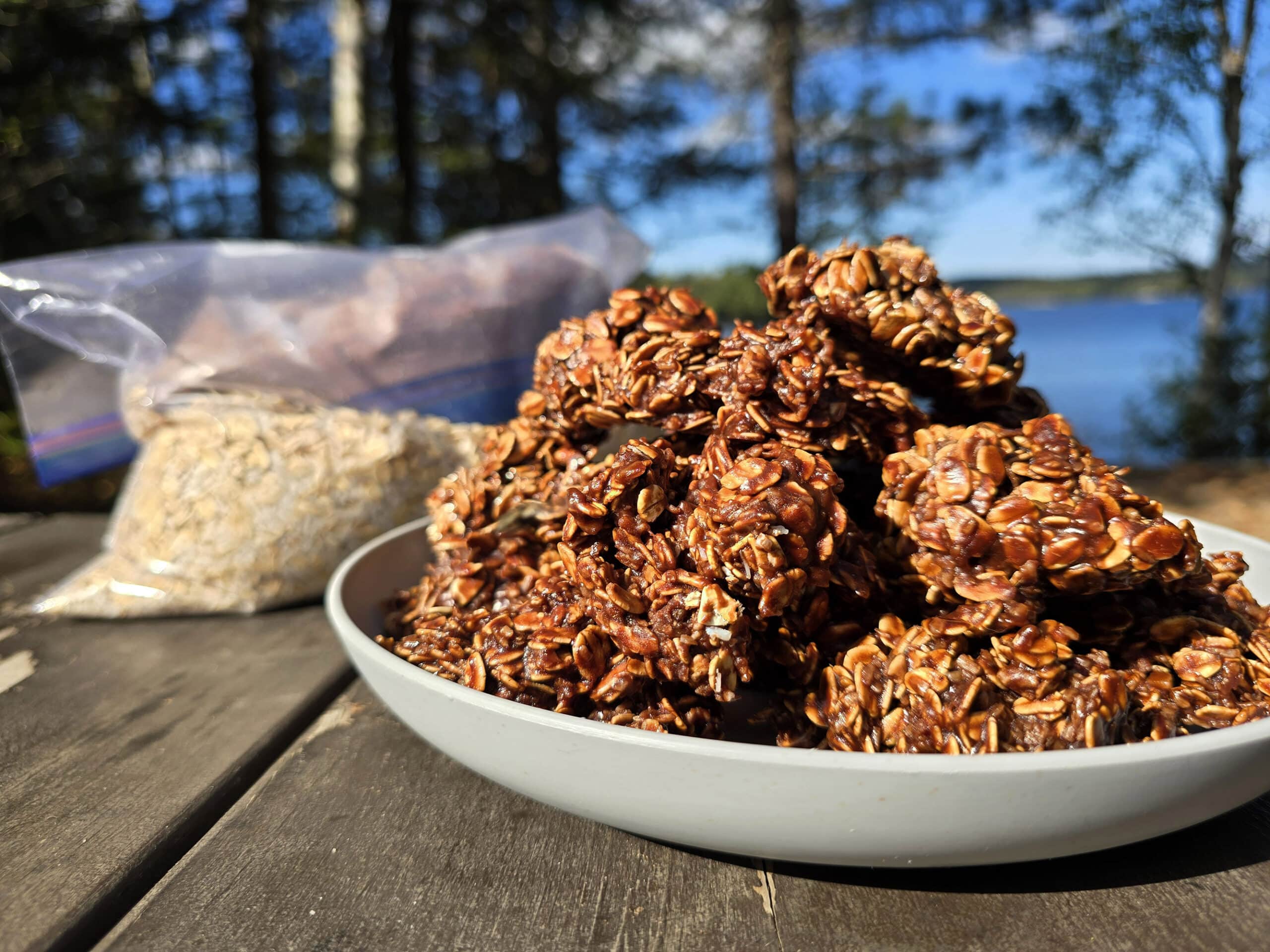 A plate of campfire chocolate haystack cookies on a picnic table, in front of a bag of homemade cookie mix.