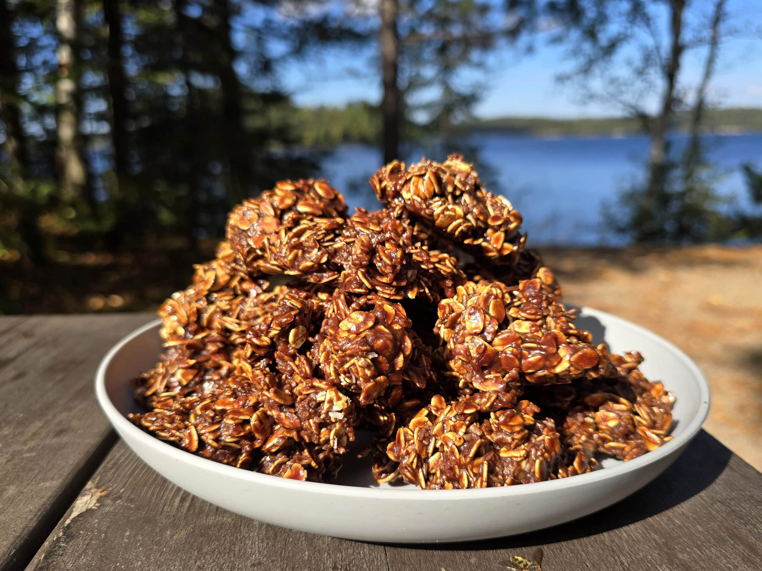 A plate of campfire haystack cookies on a picnic table, in front of a lake.