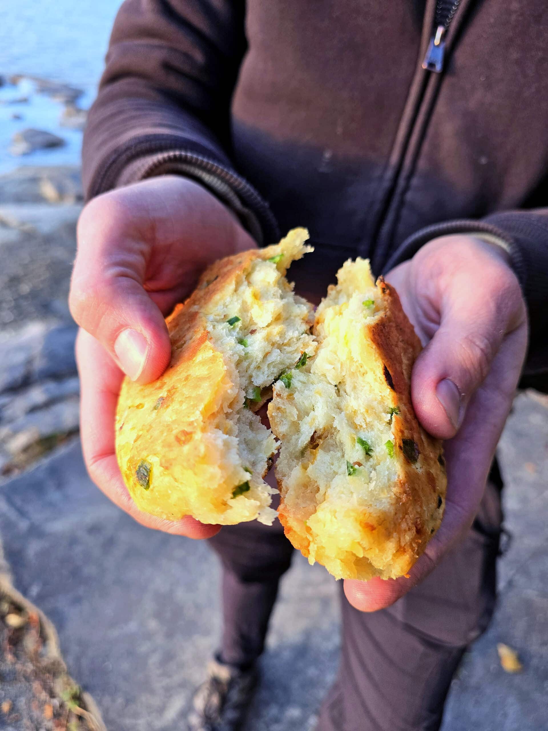 A man breaking open a piece of jalapeno cheddar bannock on a beach.