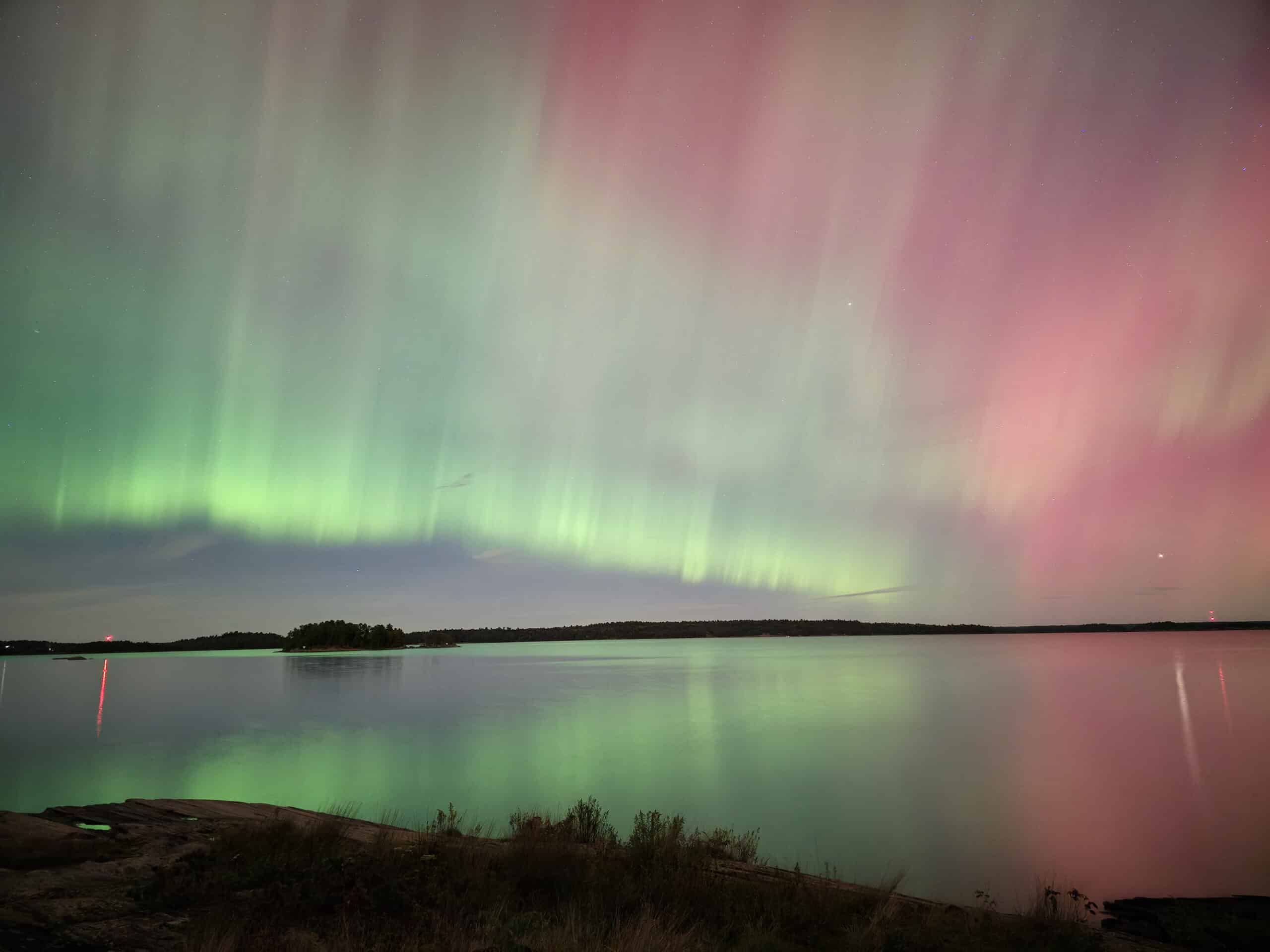 A pink and green northern lights show over a lake at Killbear Provincial Park.