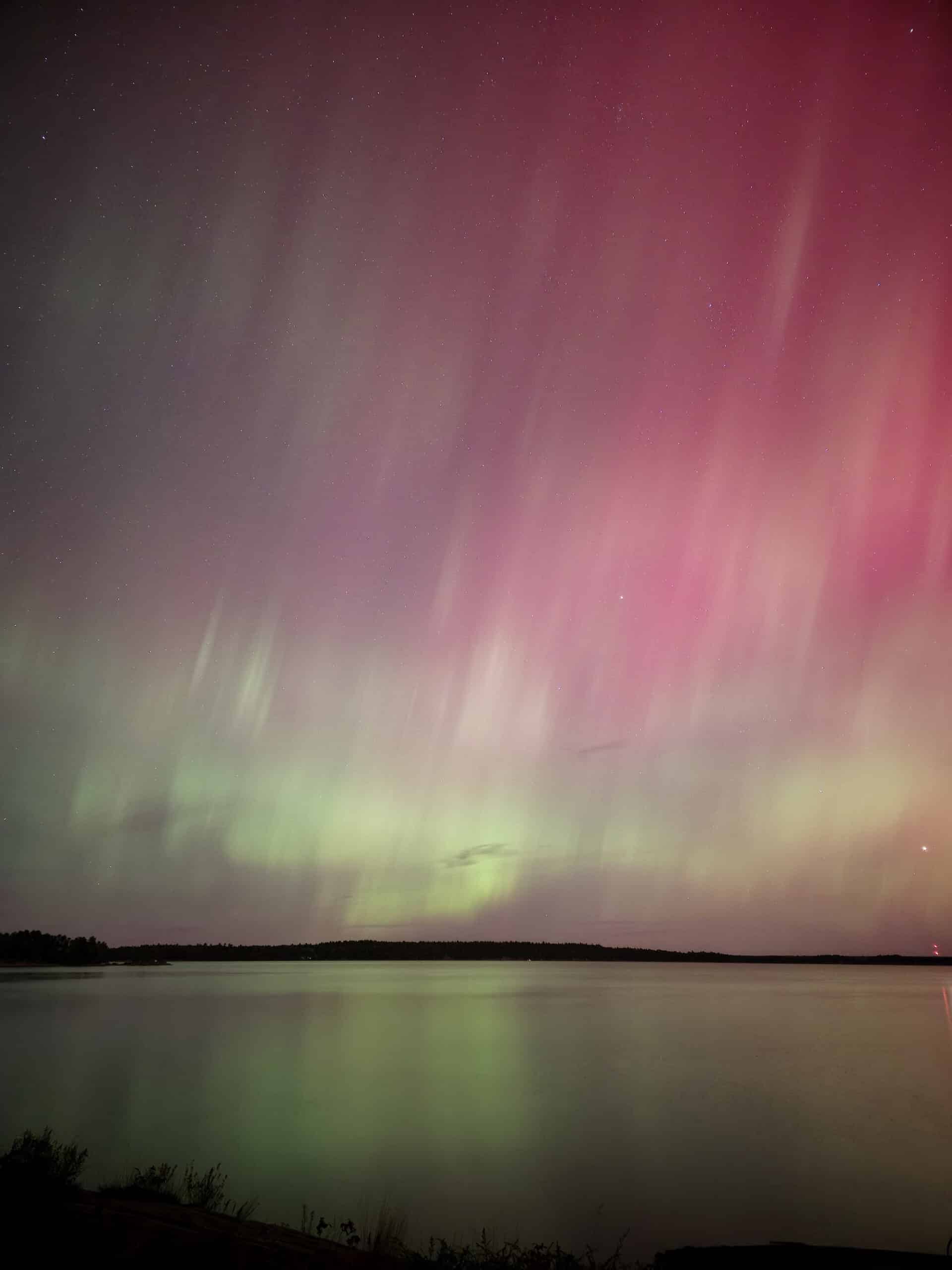 A pink and green northern lights show over a lake at Killbear Provincial Park.