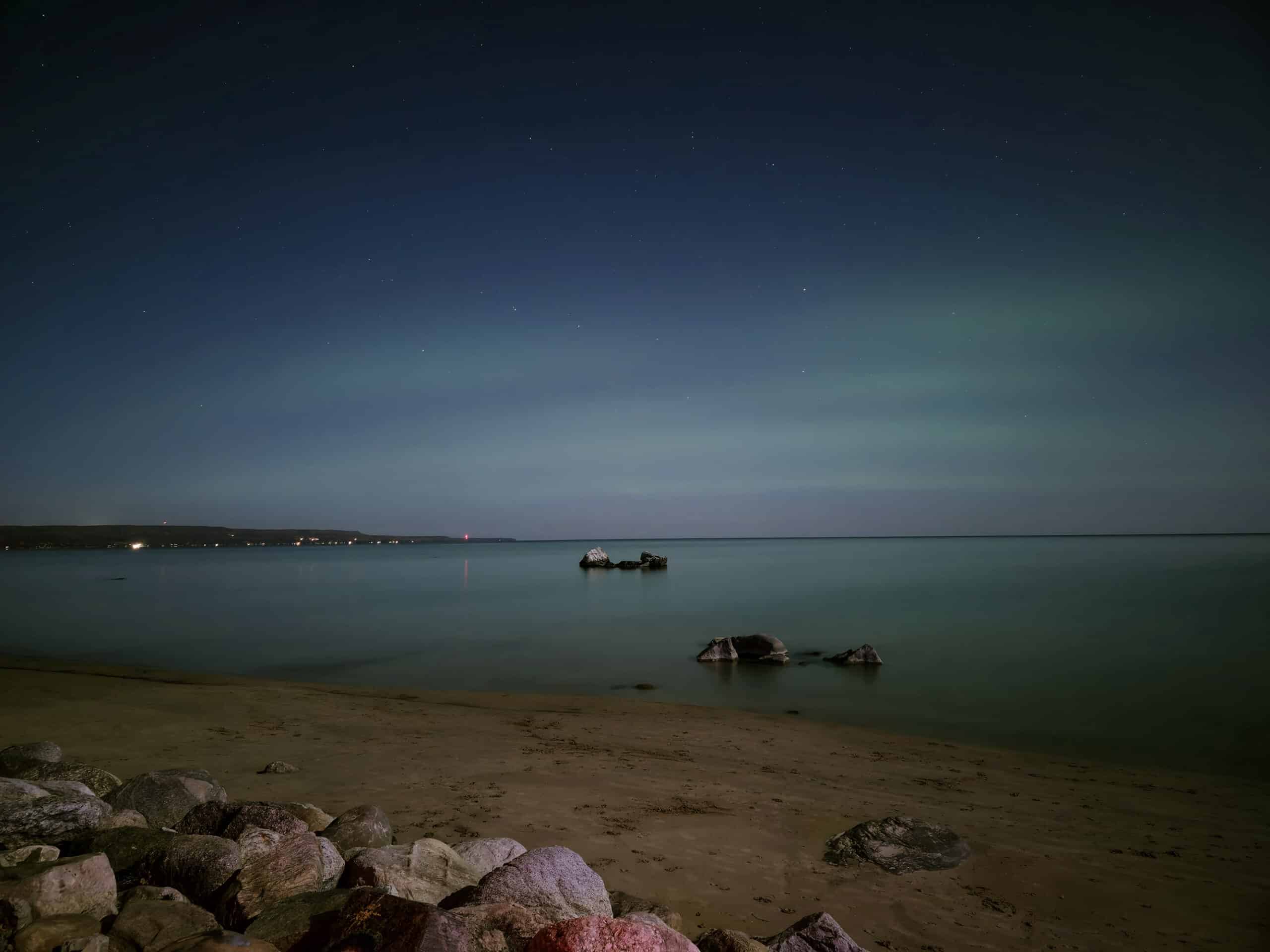 A light blue streaky aurora borealis over georgian bay, viewed from meaford memorial park.