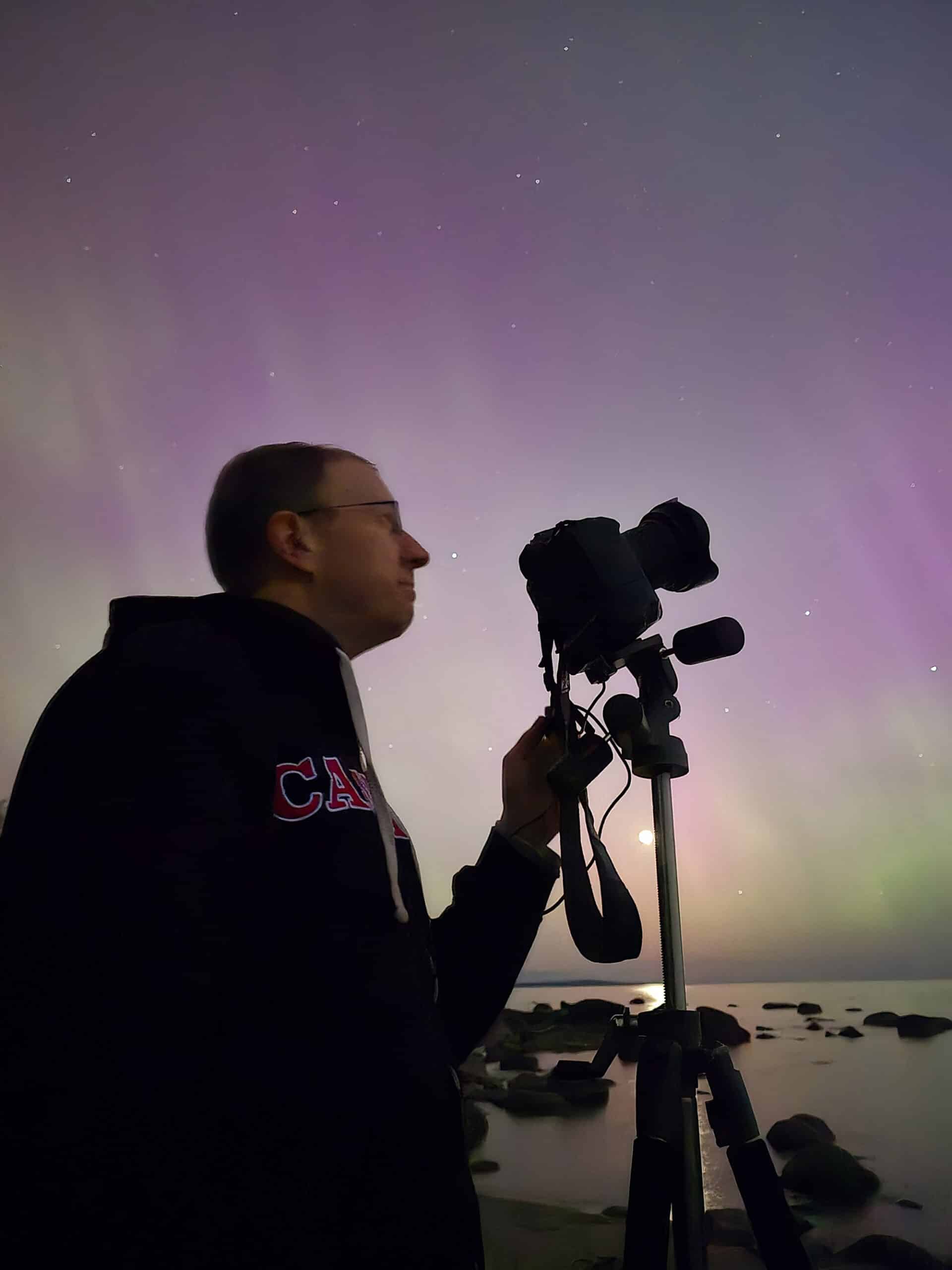 A middle aged man with a camera in front of a bright pink aurora borealis display in Ontario.