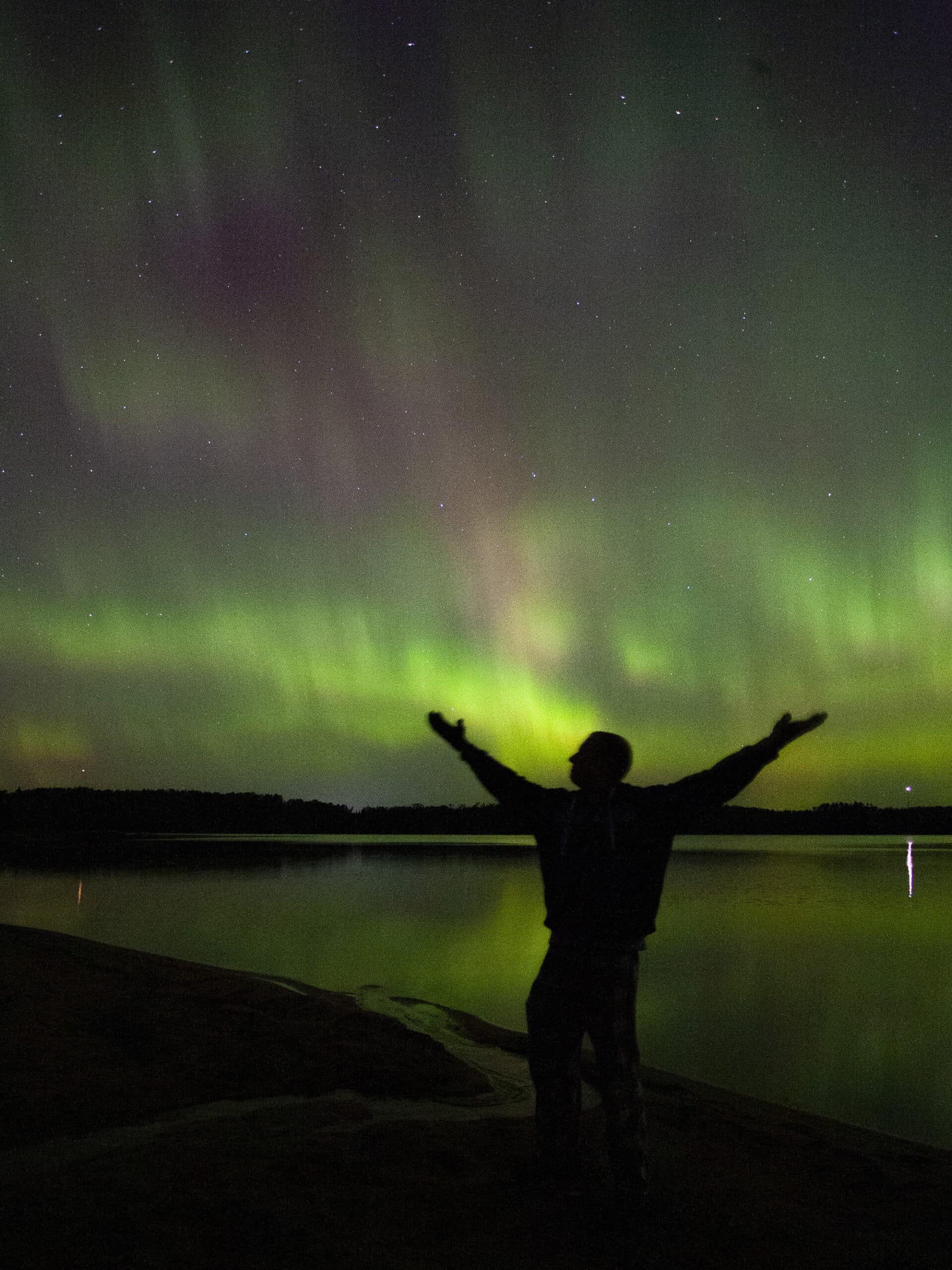 A bright northern lights display in Ontario with the silhouette of a man in front.