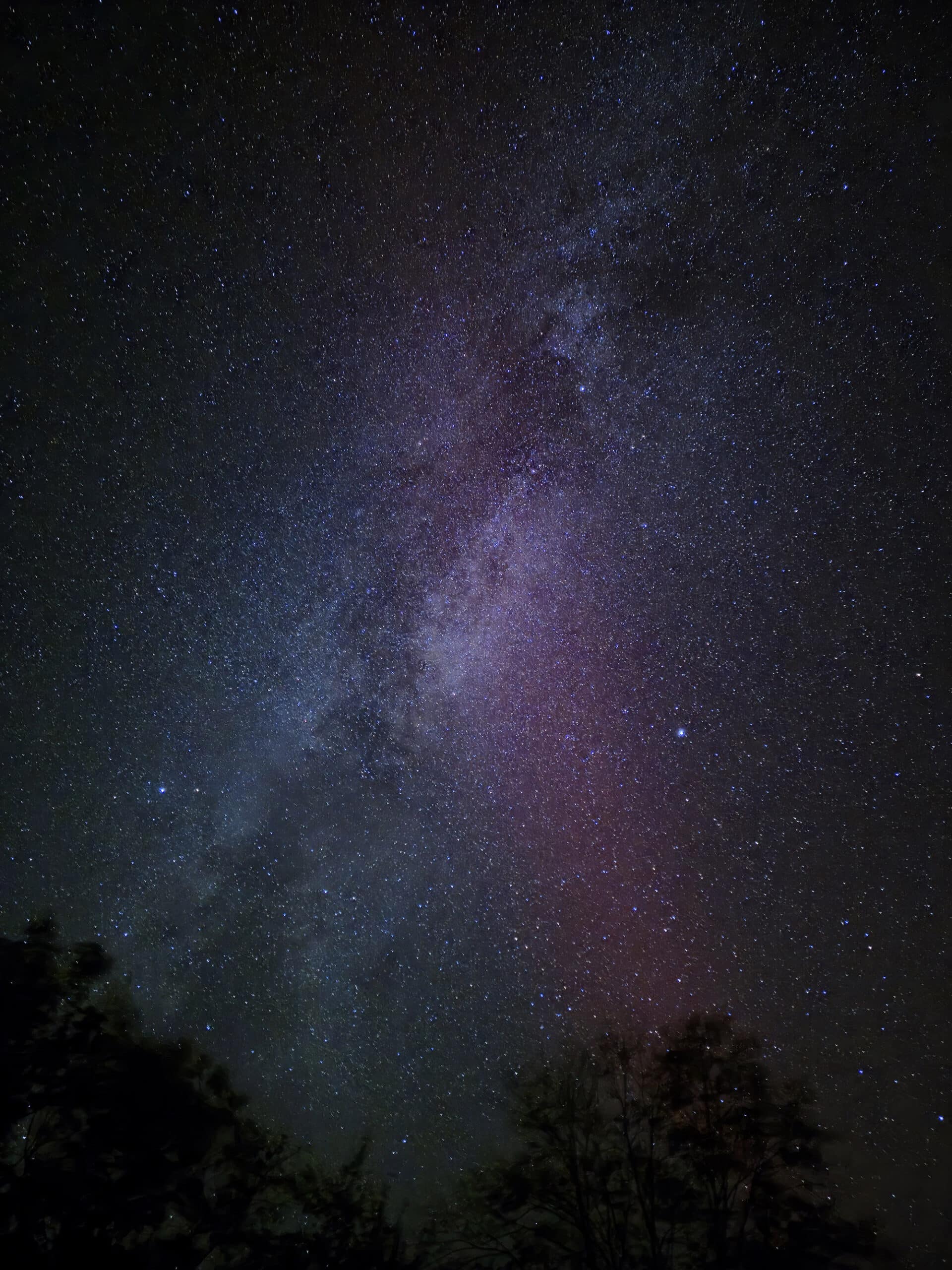 A photo of the milky way, with a magenta strip of aurora borealis crossing through it.