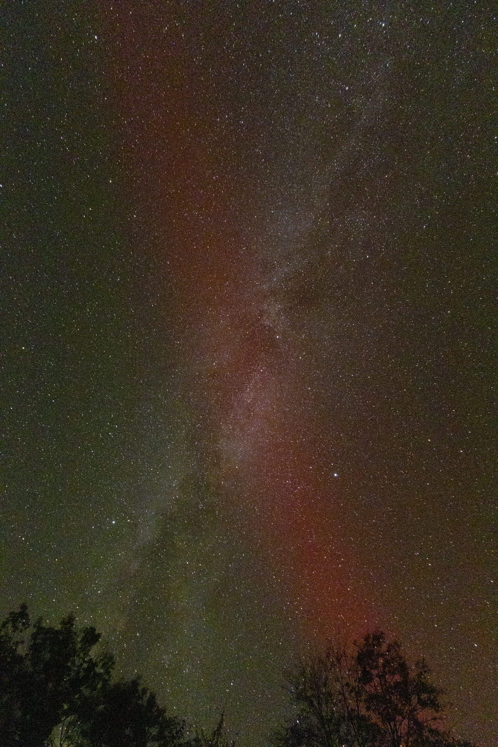 A photo of the Milky Way in the sky, a somewhat straight line, and a red aurora borealis line forming an X shape with the Milky Way.