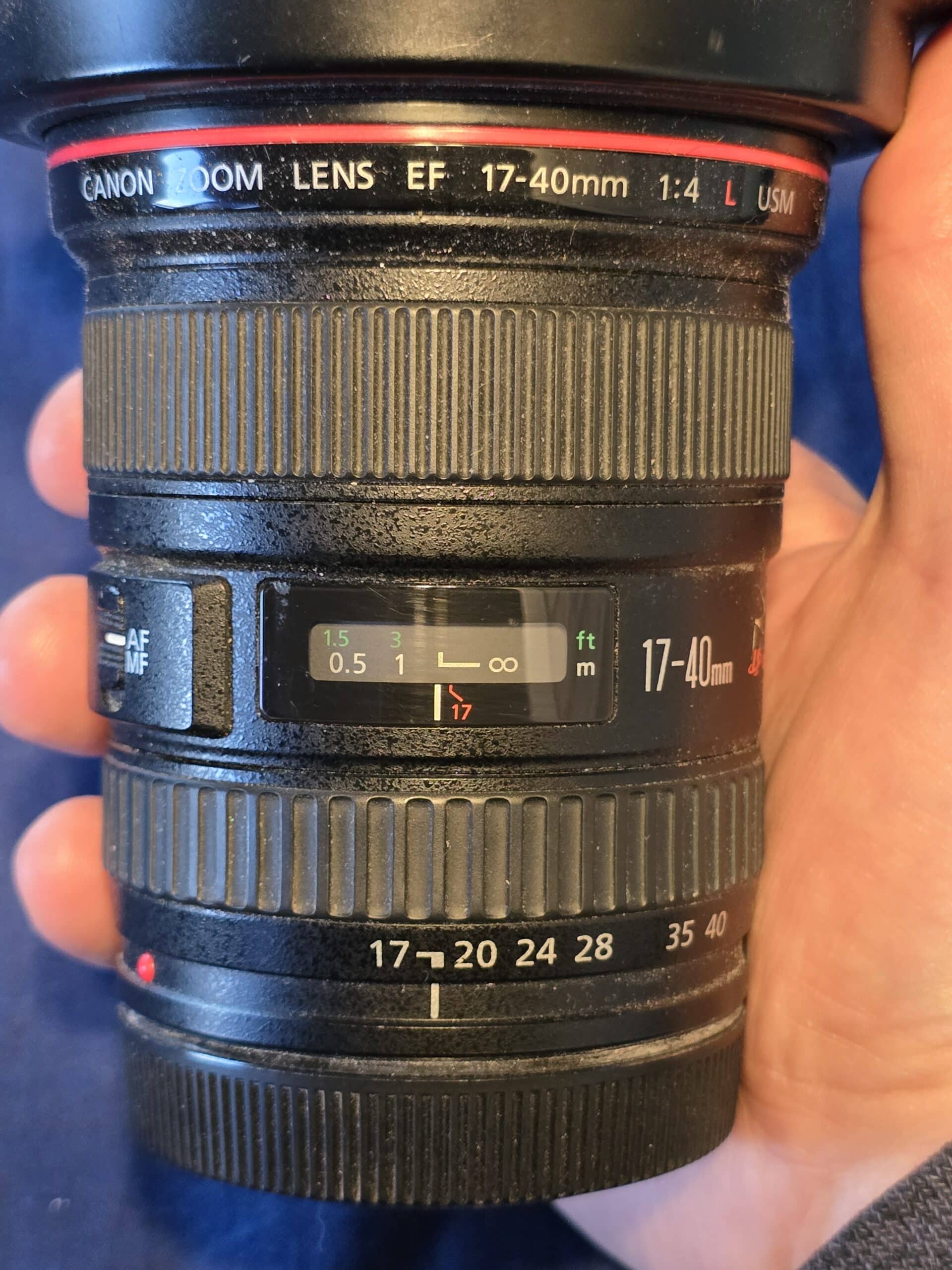 A hand holding a camera lens.  The focus is set just a little to the left of the infinity line.