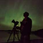 The silhouette of a man with a camera in front of the northern lights.