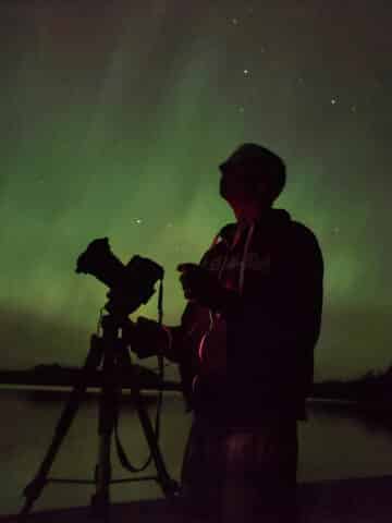 The silhouette of a man with a camera in front of the northern lights.