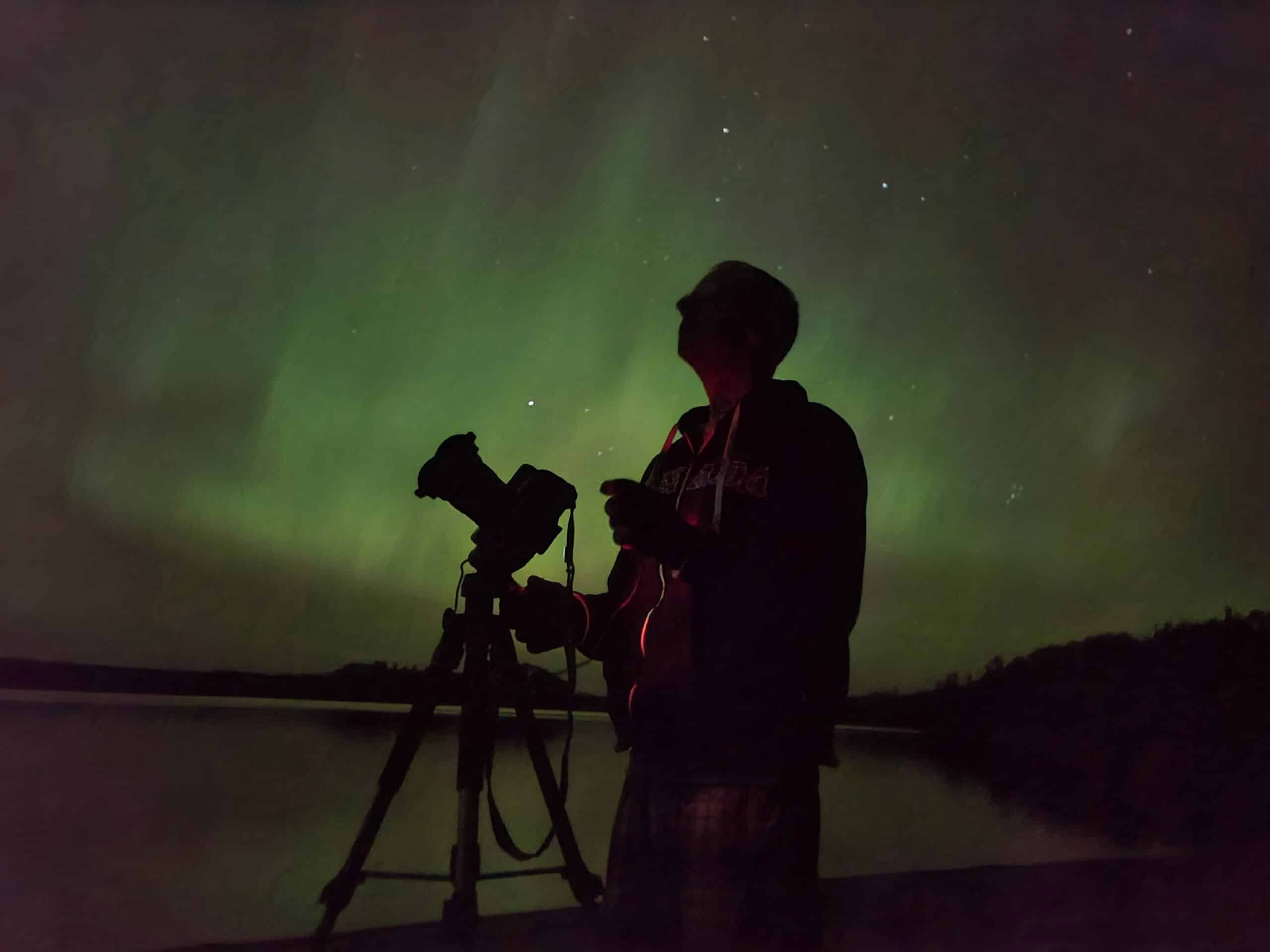 The silhouette of a man with a camera in front of the northern lights.