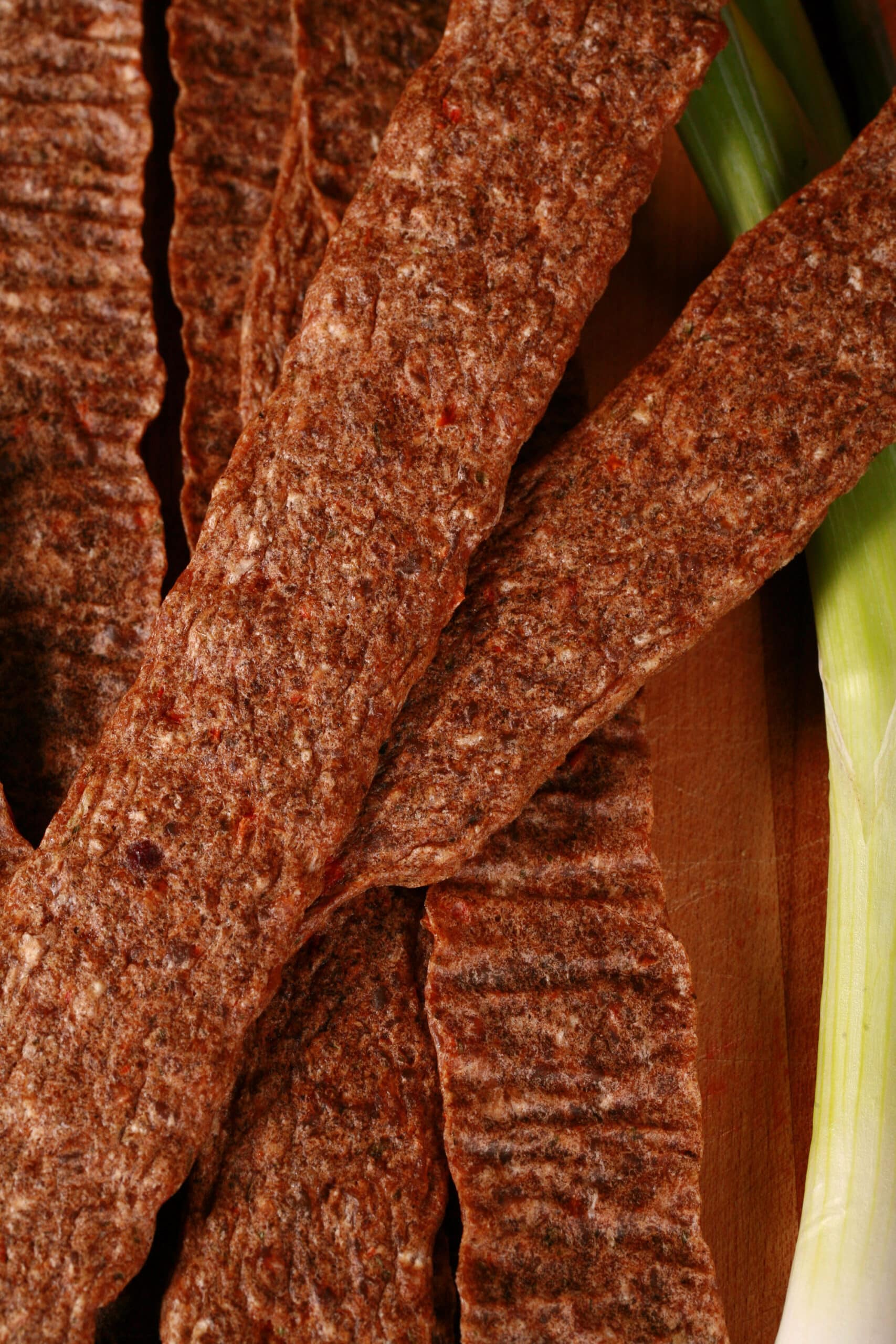 Several strips of Jamaican jerk chicken jerky on a cutting board, with green onions and scotch bonnet peppers.